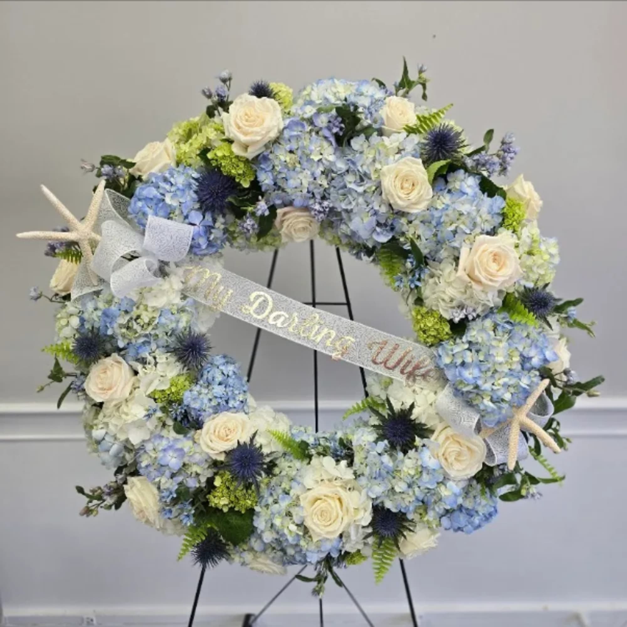 Circular floral wreath with blue hydrangeas, white roses, and starfish accents