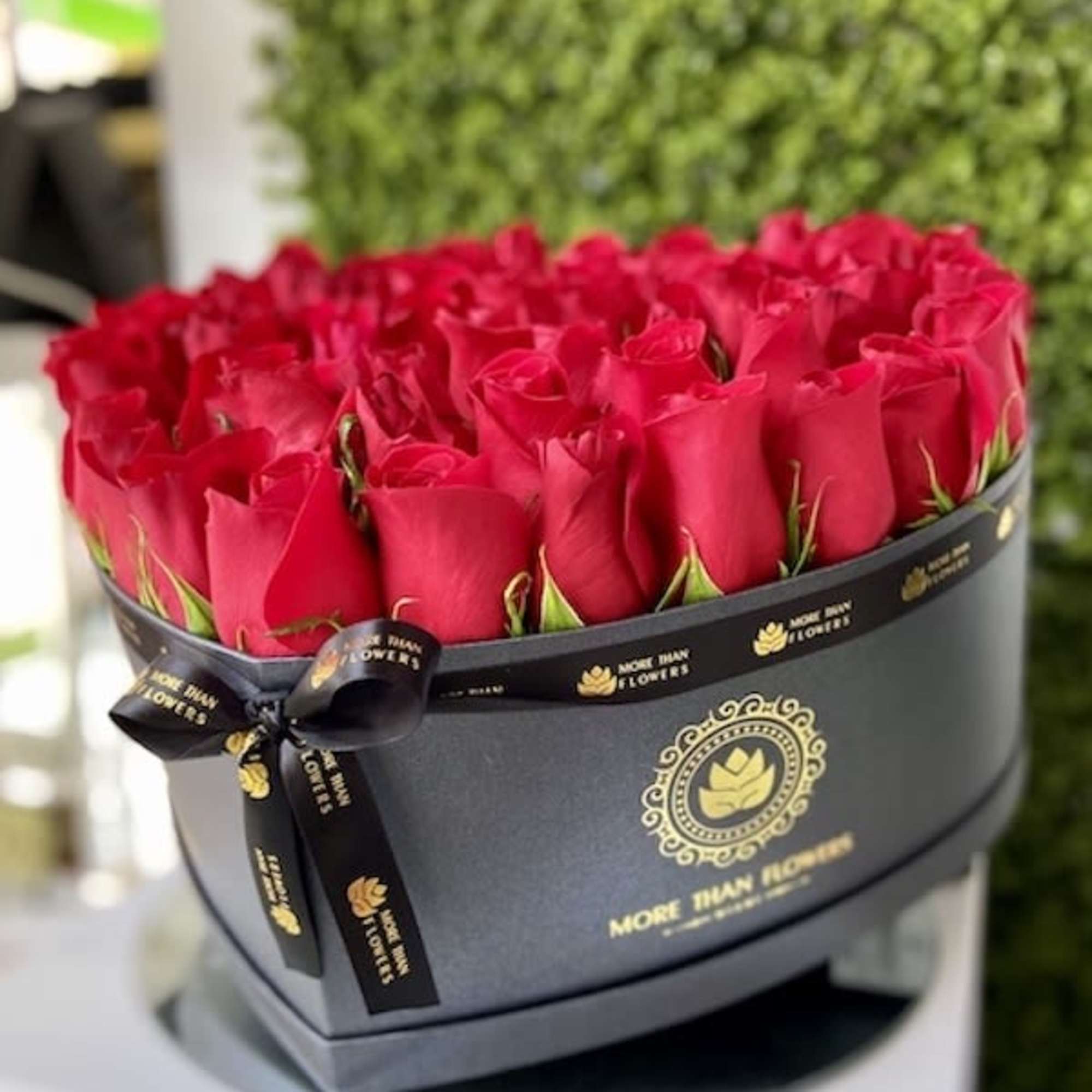 Heart-shaped black box filled with tightly packed red roses and a black logo ribbon