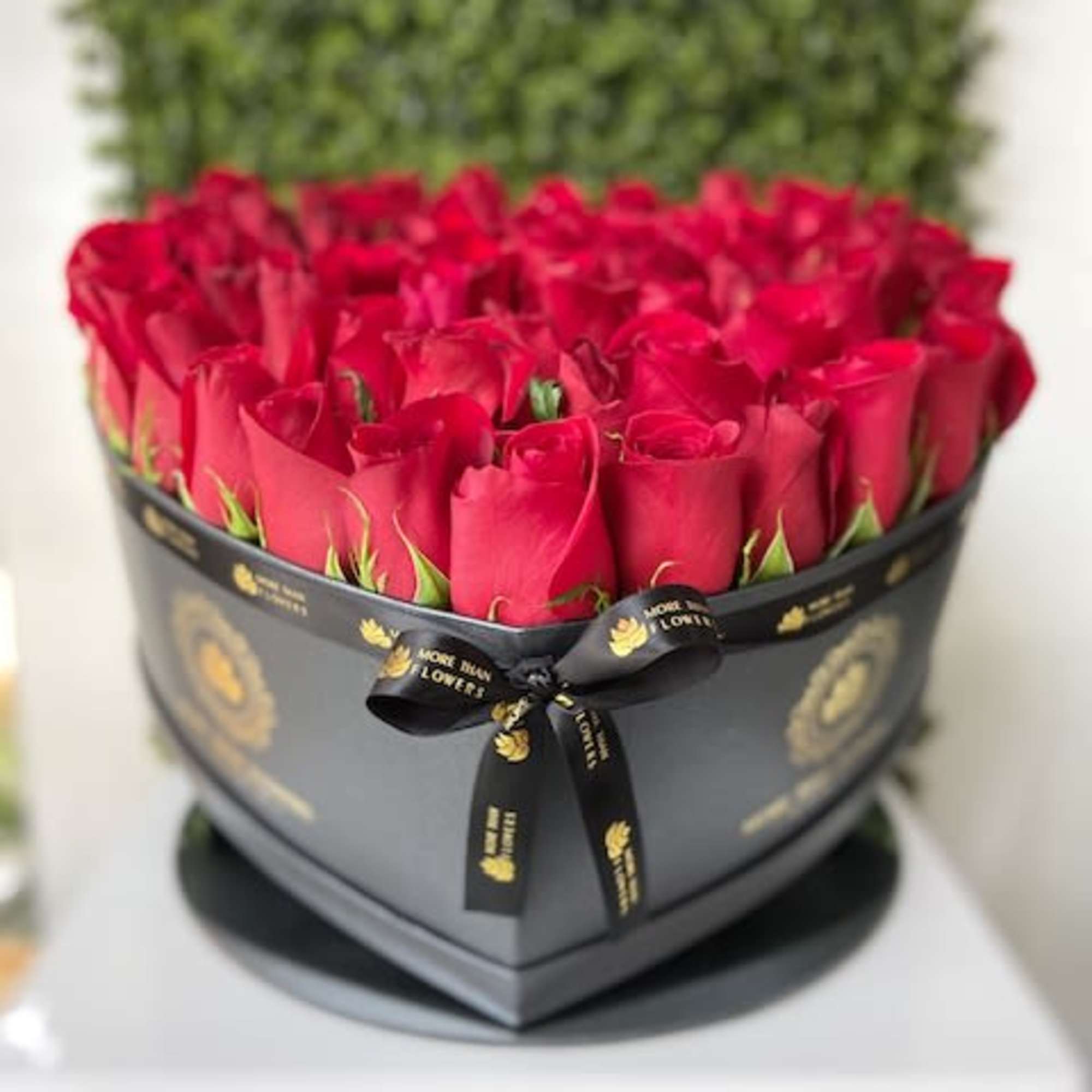 Heart-shaped black box filled with red roses and tied with a black logo ribbon