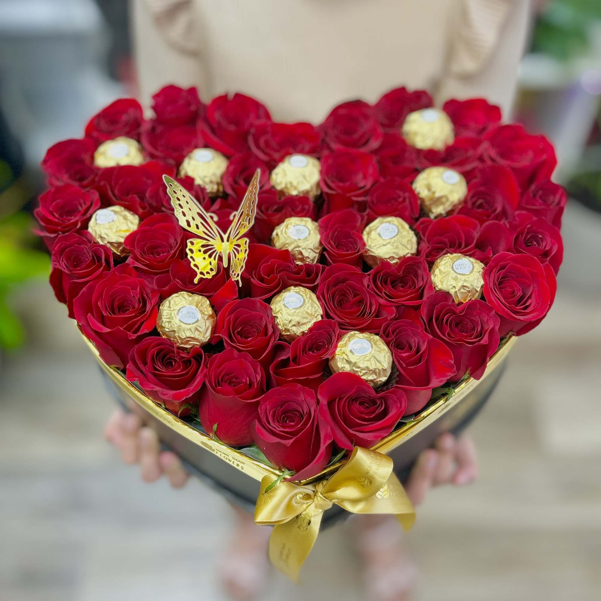Heart-shaped box of red roses with gold-wrapped chocolates and a gold ribbon bow