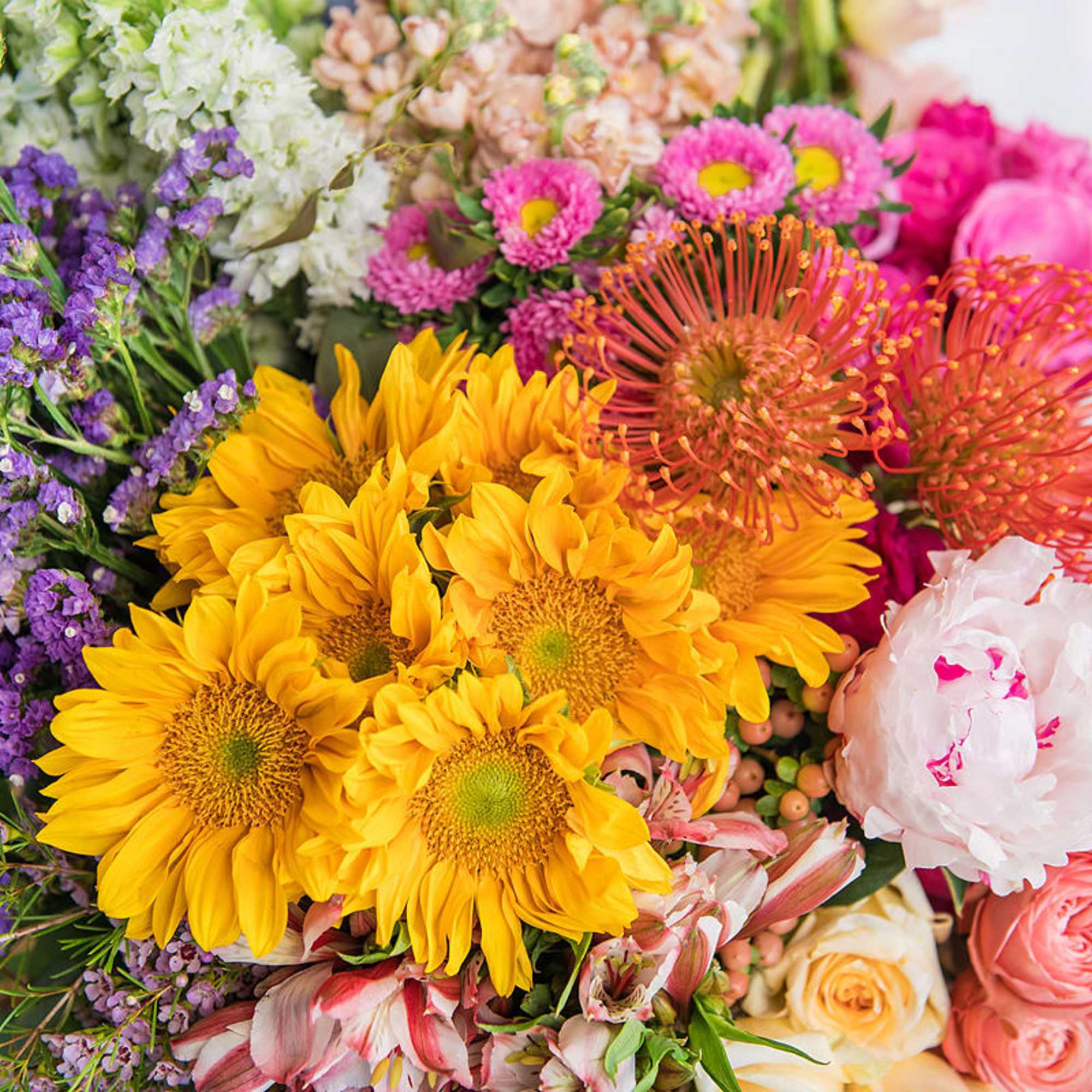 Bright mixed bouquet with yellow sunflowers, pink peonies, roses, and assorted colorful blooms