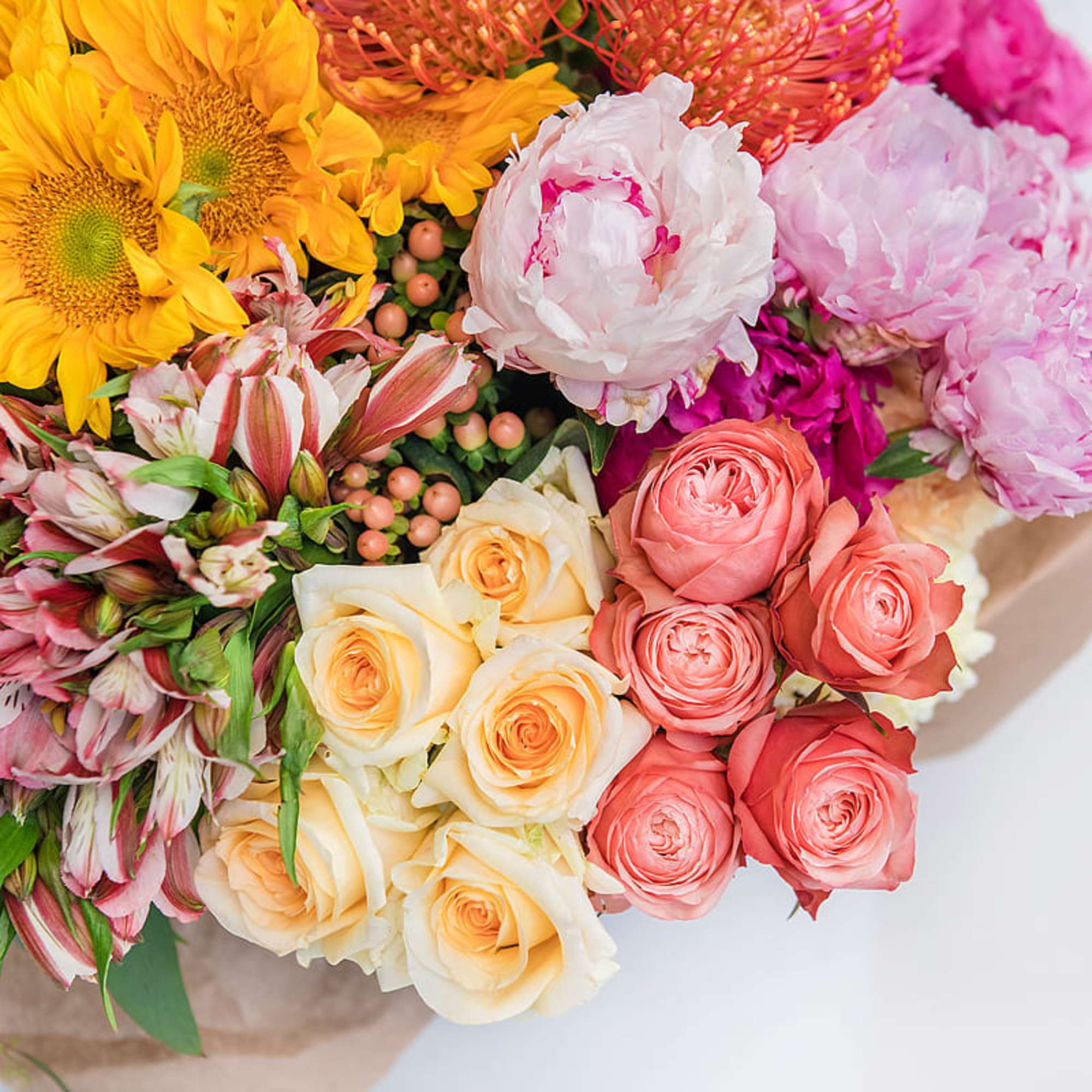 Colorful bouquet with sunflowers, peonies, roses, alstroemeria, and protea wrapped in kraft paper