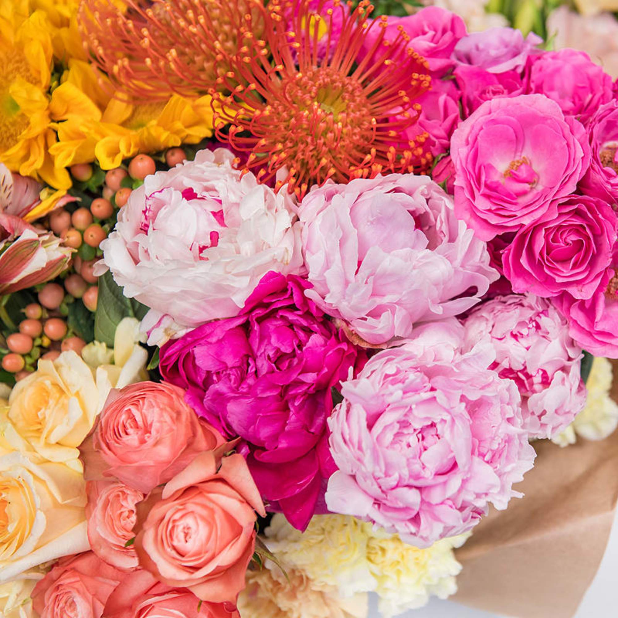 Bright mixed bouquet with pink peonies, roses, orange protea, and yellow blooms in kraft paper wrap