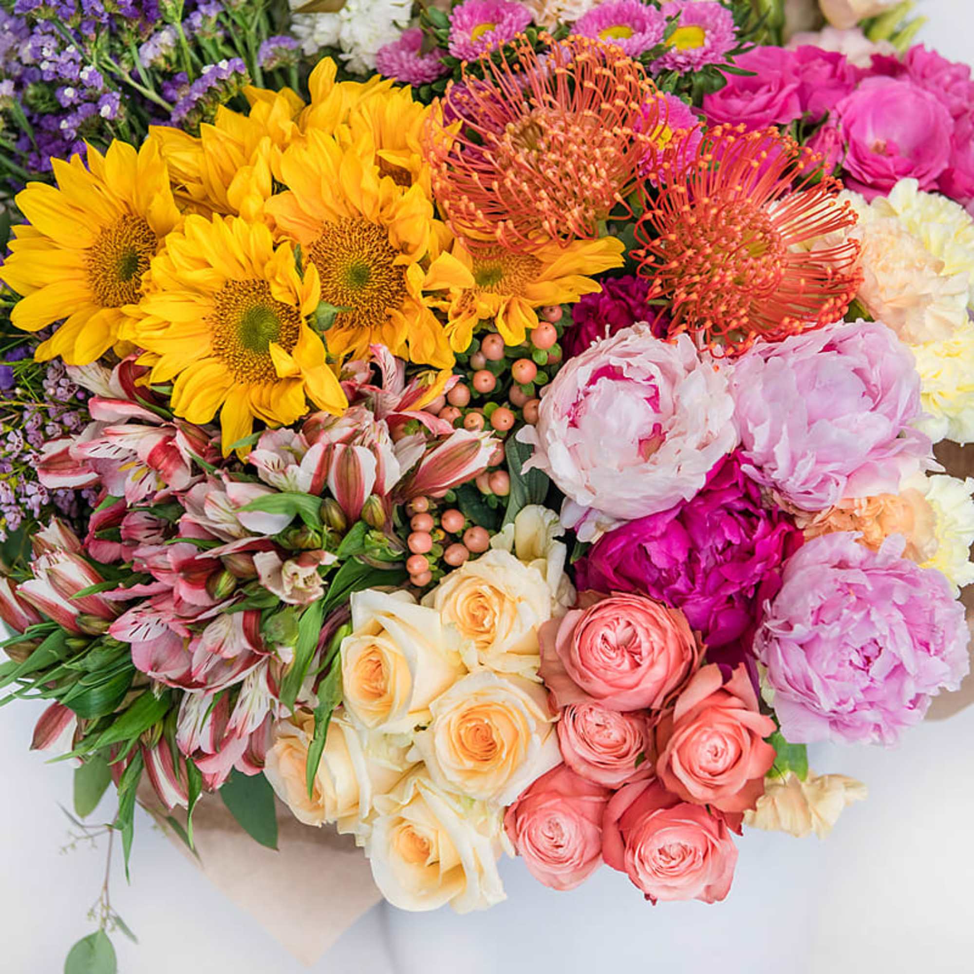 Vibrant mixed bouquet with sunflowers, roses, peonies, protea, and alstroemeria in pink, yellow, and peach tones
