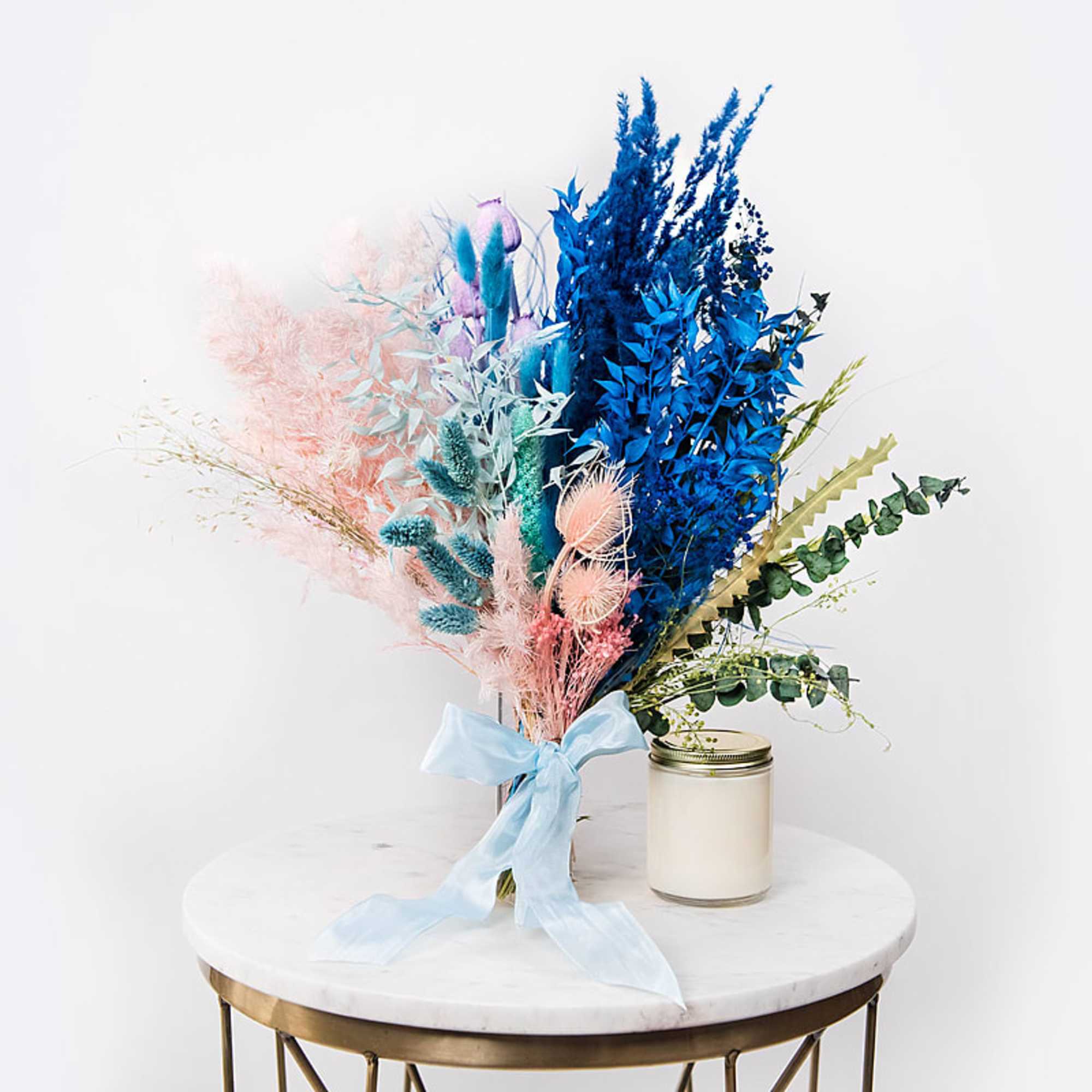 Colorful dried bouquet with a blue ribbon beside a white candle jar