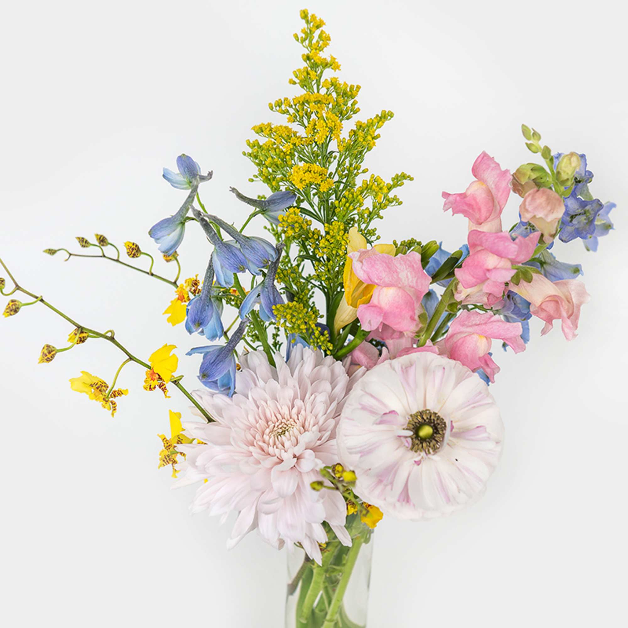 Tall mixed bouquet with pink snapdragons, blue delphinium, yellow blooms and pale mums in a clear glass vase
