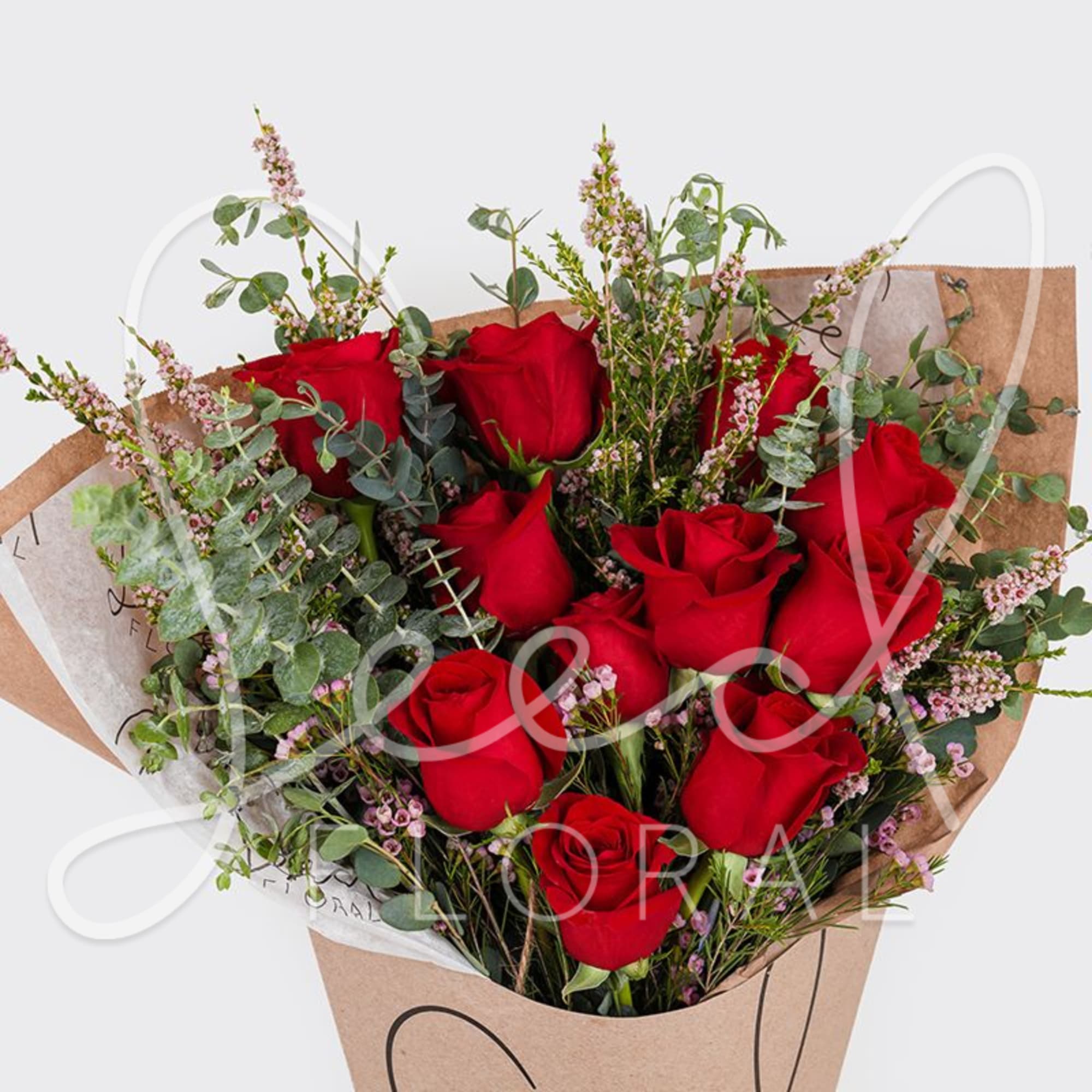 Hand-tied bouquet of red roses with pink filler flowers wrapped in brown kraft paper