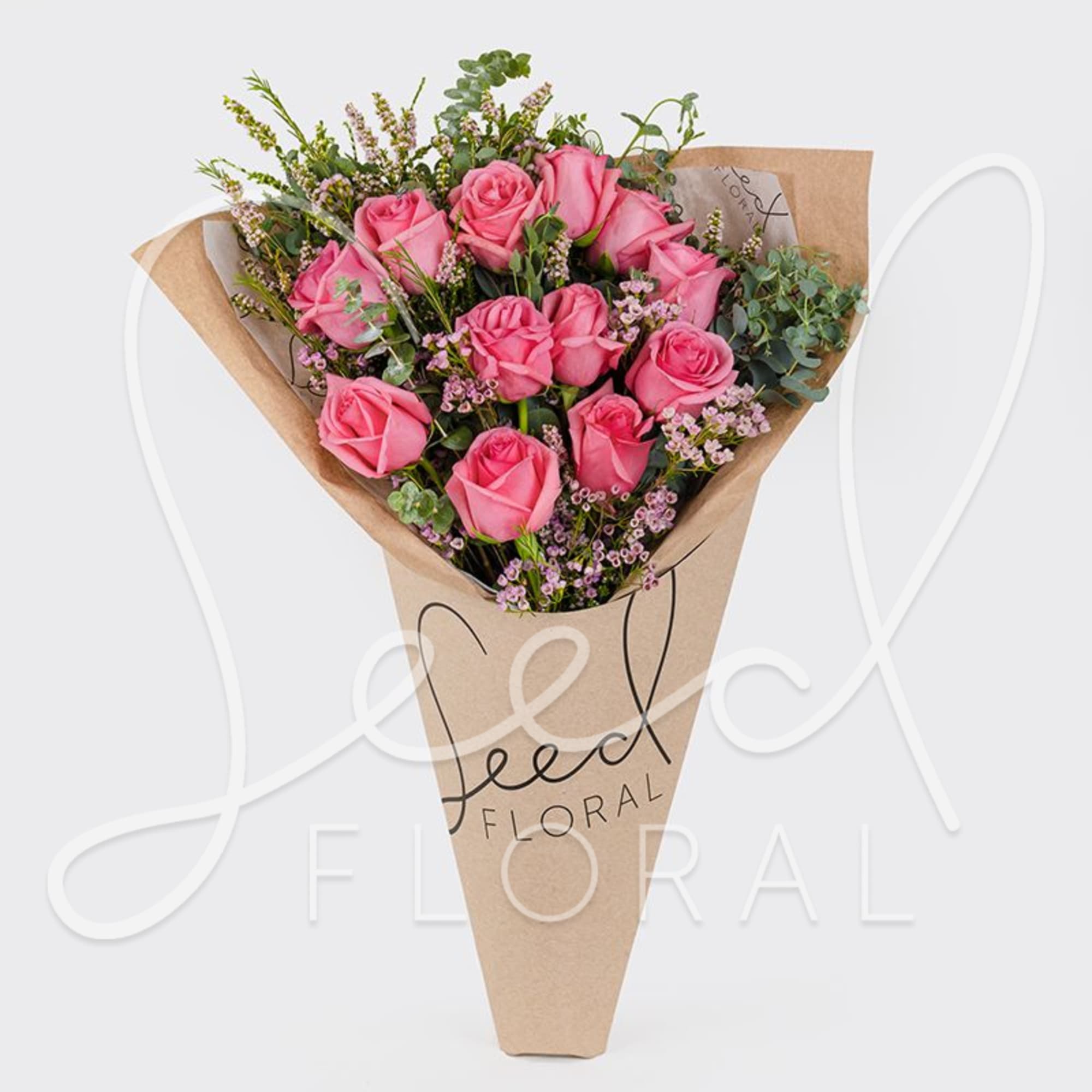 Bouquet of pink roses with small pink filler flowers wrapped in a kraft paper sleeve