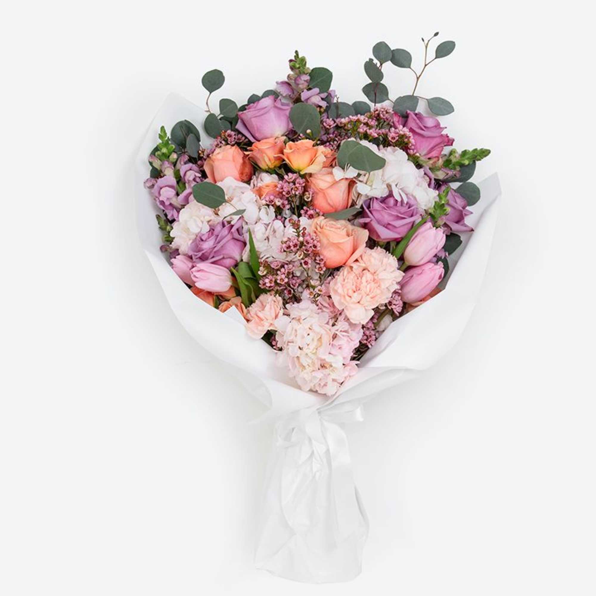 Hand-tied bouquet of peach and lavender roses with pink tulips and carnations in white wrap
