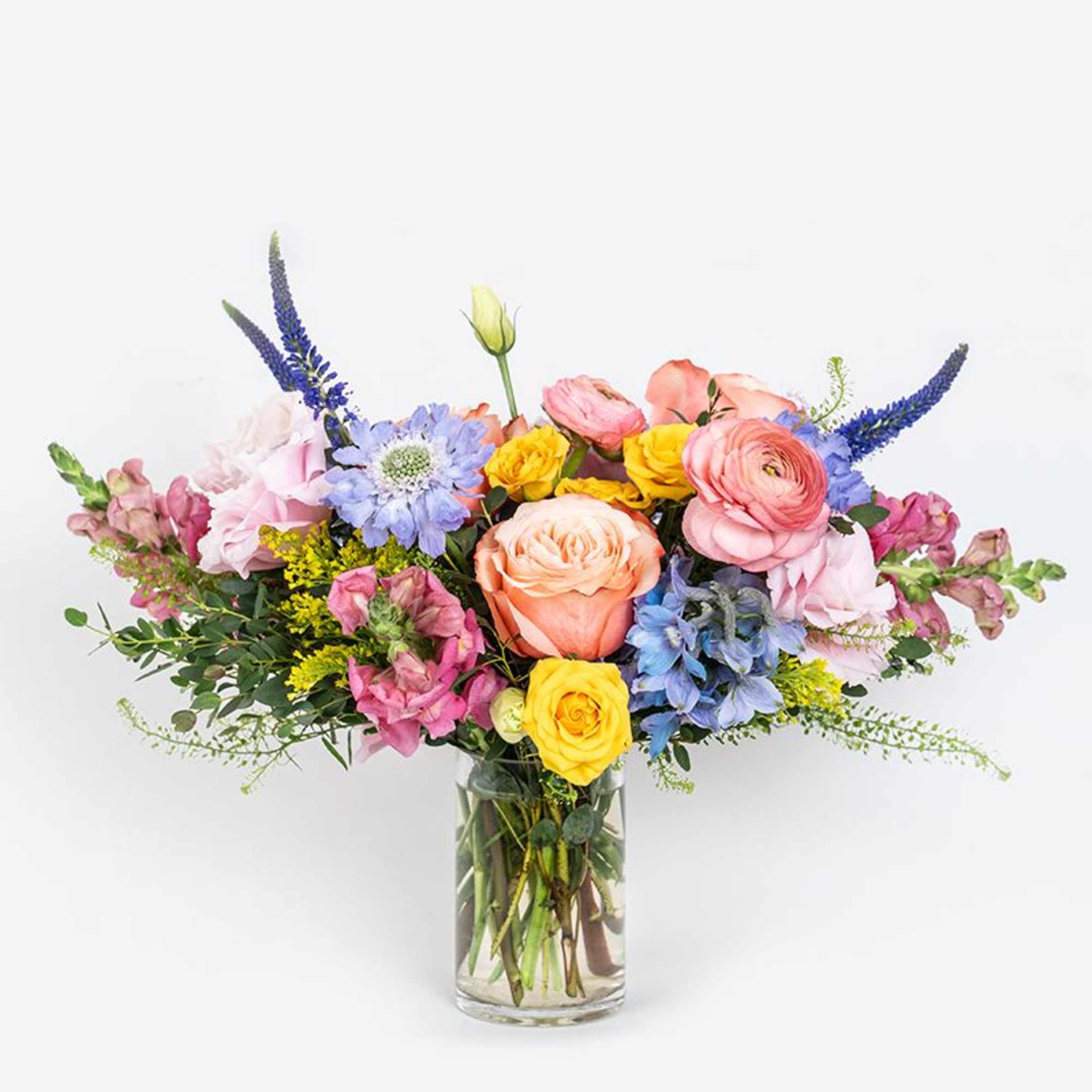 Mixed bouquet of pink, peach, yellow, and blue flowers in a clear glass vase