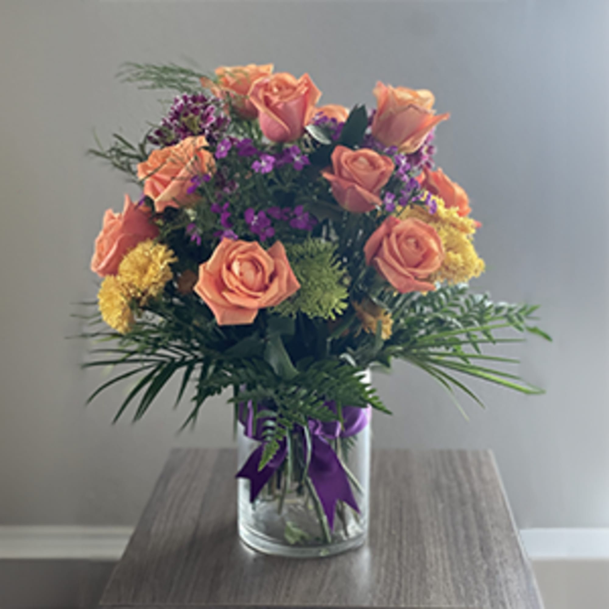Peach roses in a glass vase with purple filler flowers