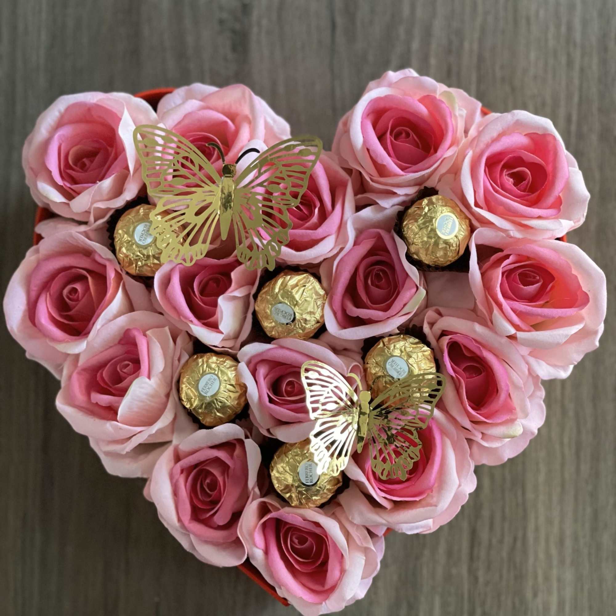 Heart-shaped box of pink roses with gold-wrapped chocolates and butterfly picks