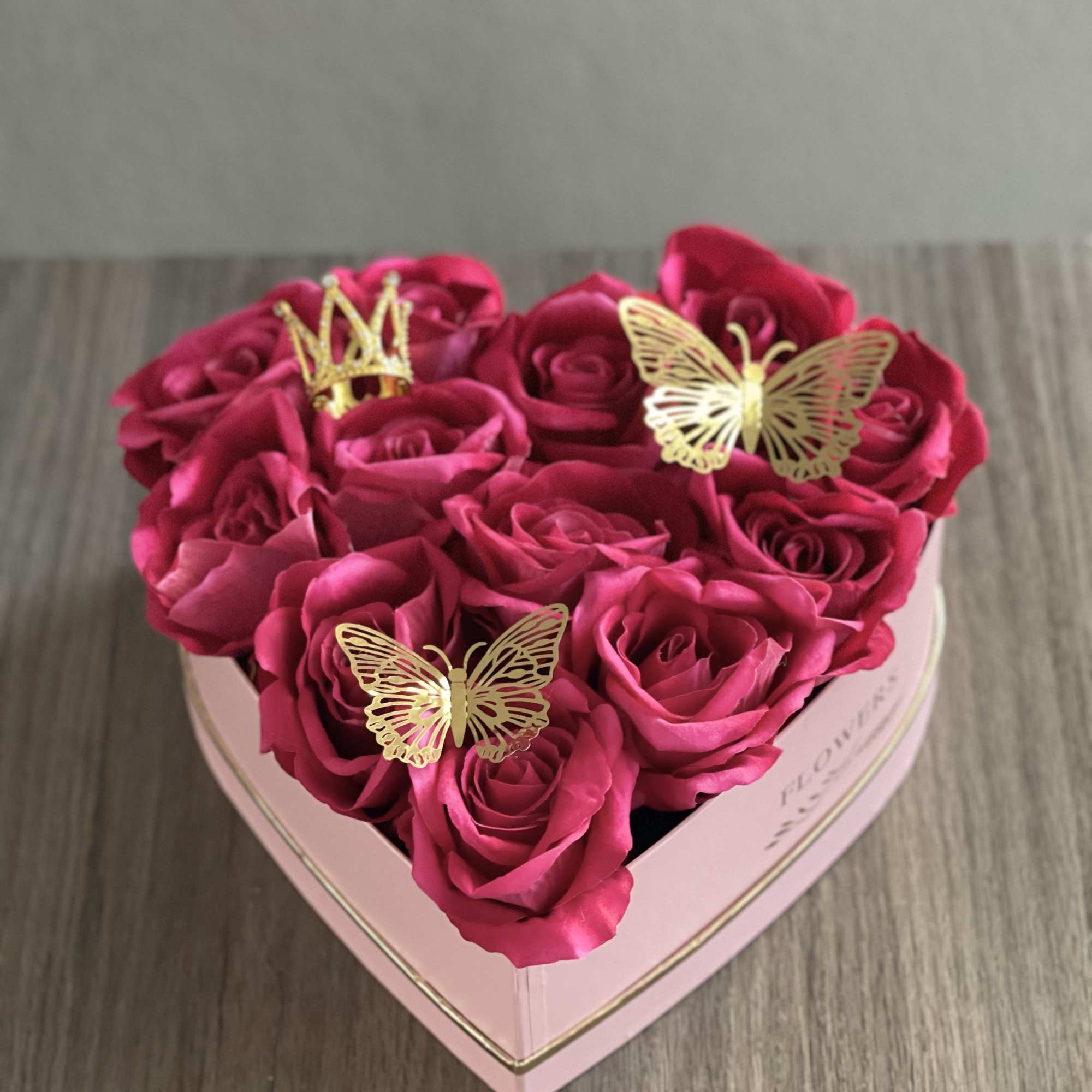 Heart-shaped pink box filled with hot pink roses and gold butterfly toppers