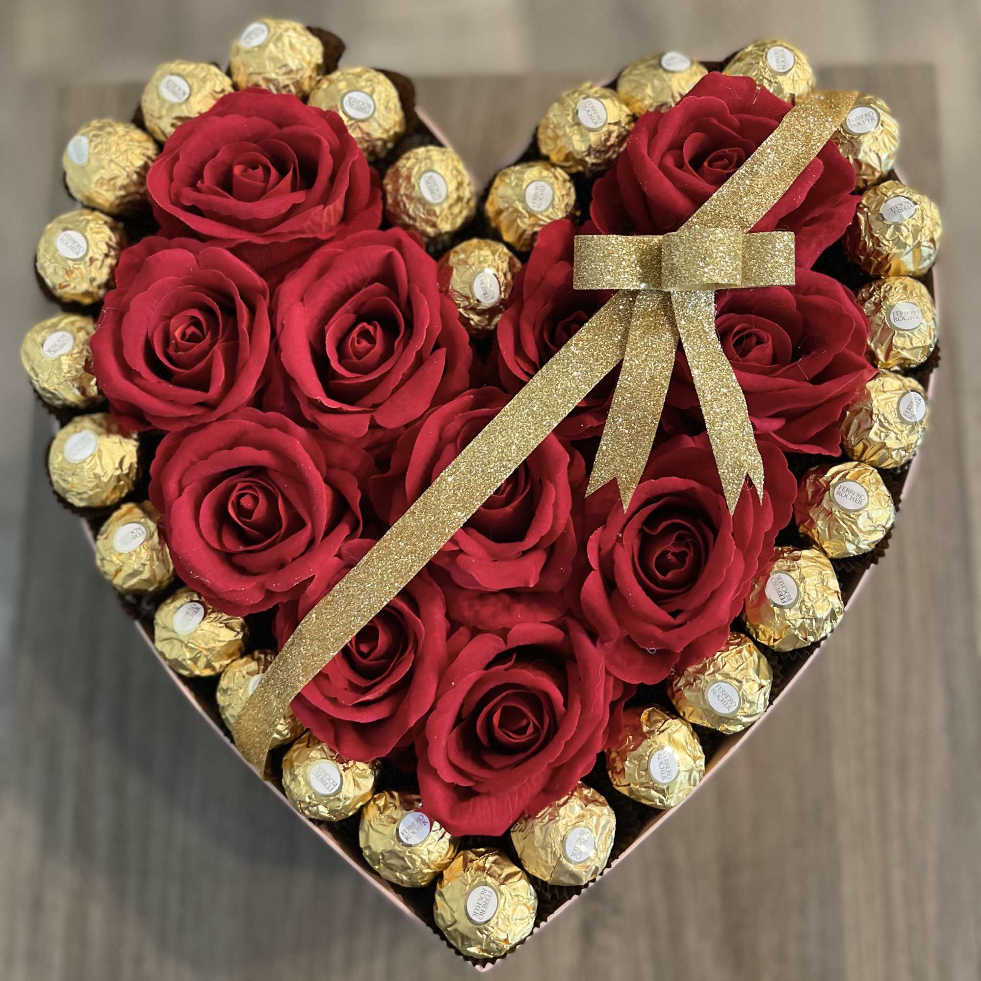 Heart-shaped box with red roses and gold-wrapped chocolates tied with a glitter ribbon