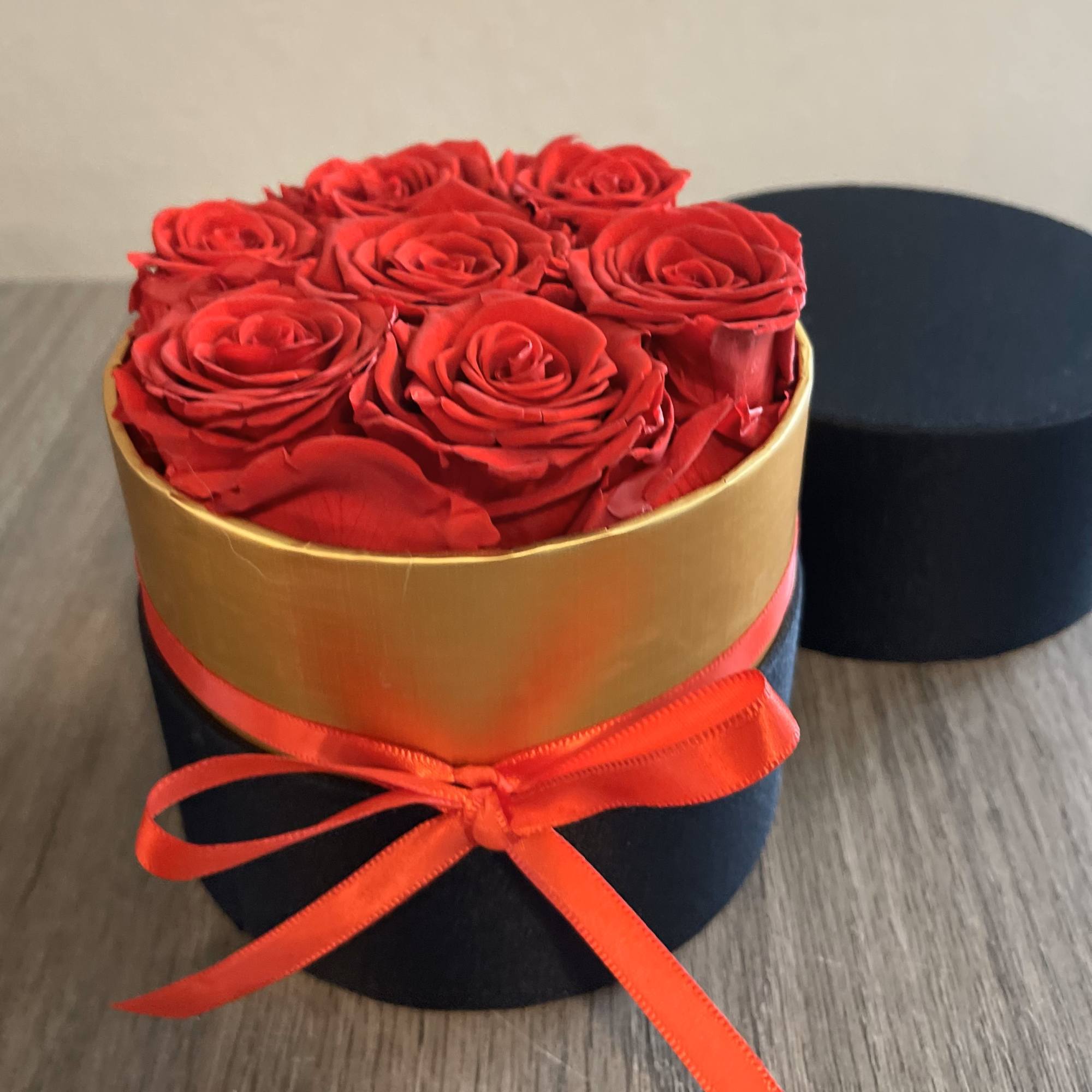 Red roses arranged in a round black box with a gold band and red ribbon