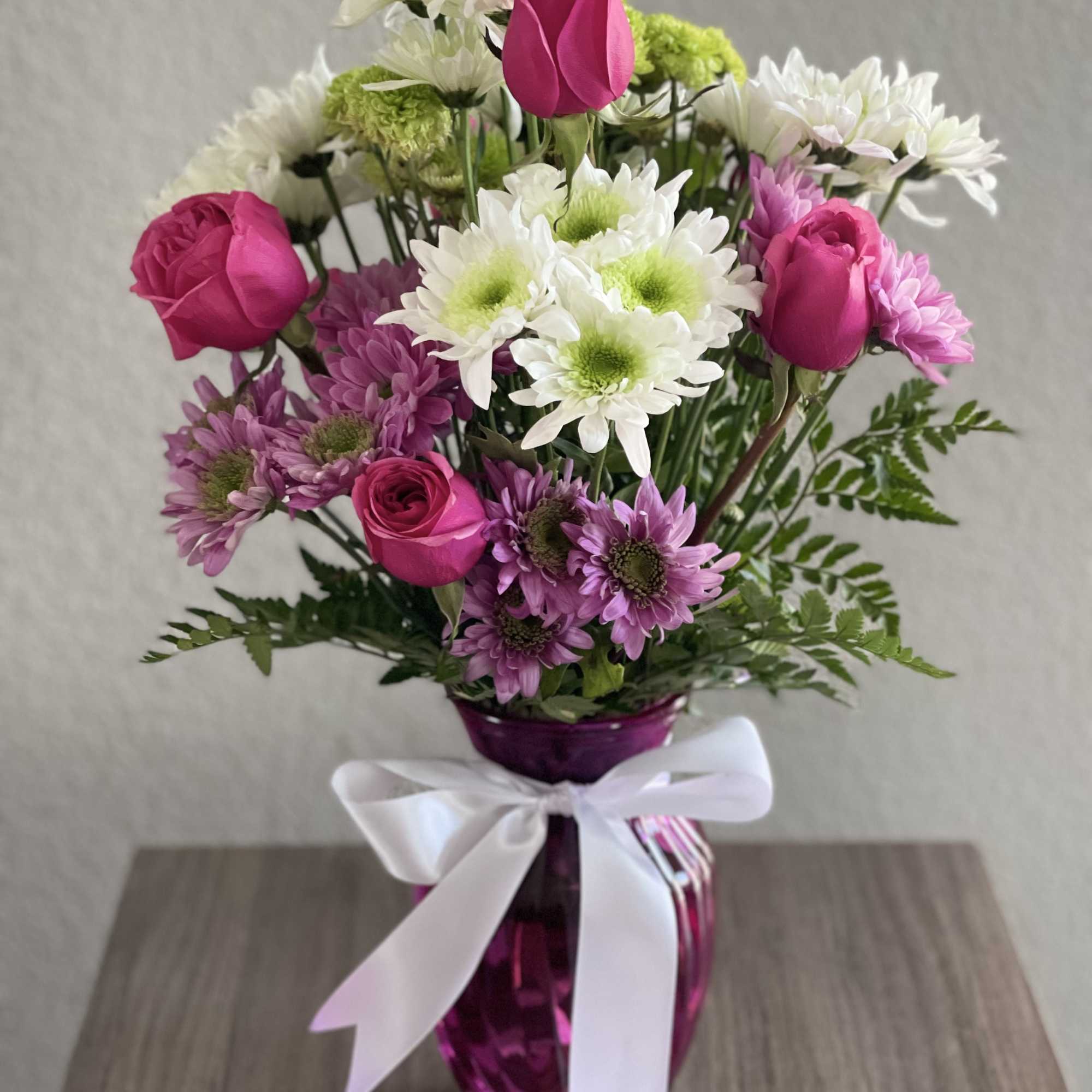 Pink roses and white daisies in a purple vase with a white ribbon