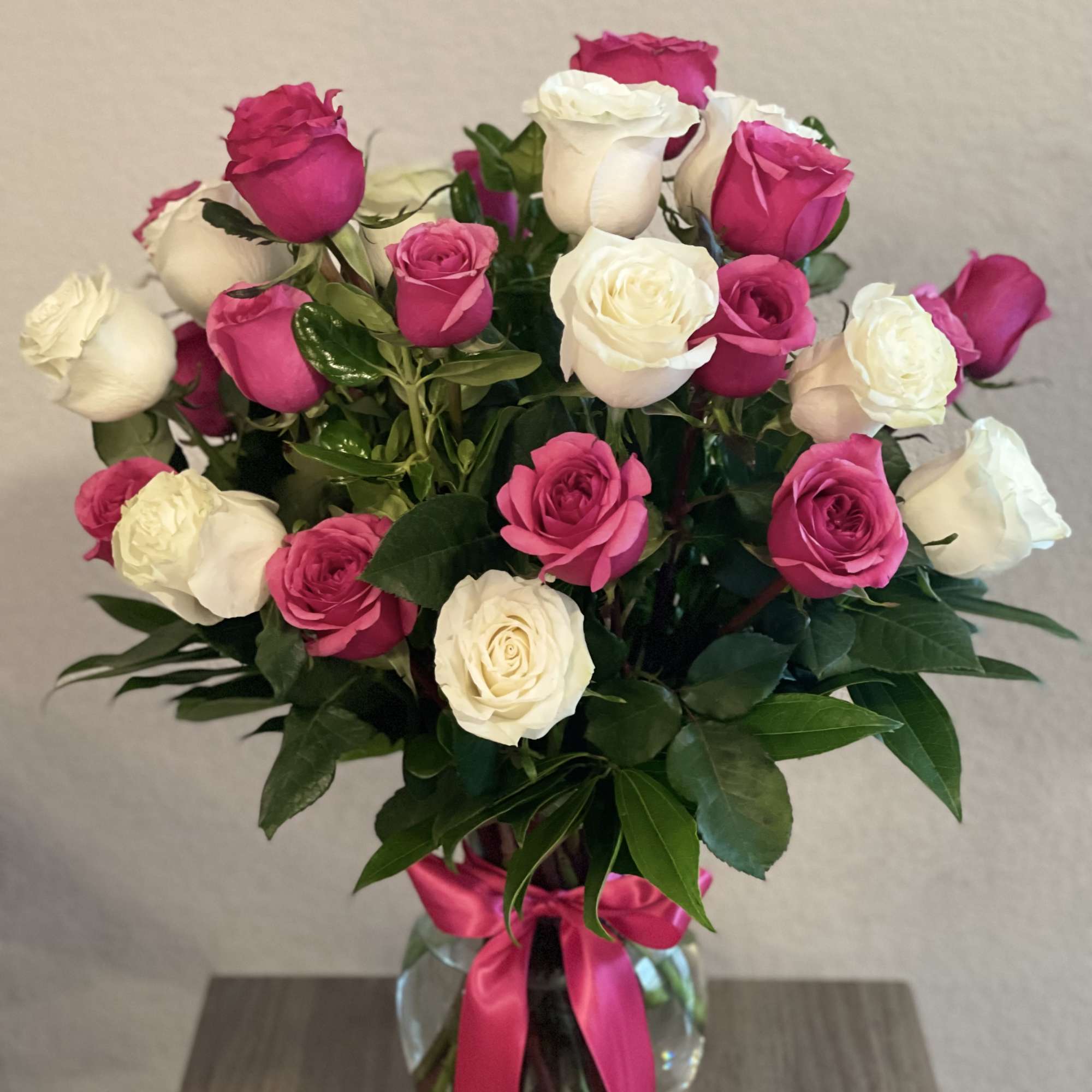 Bouquet of pink and white roses in a glass vase with a pink ribbon
