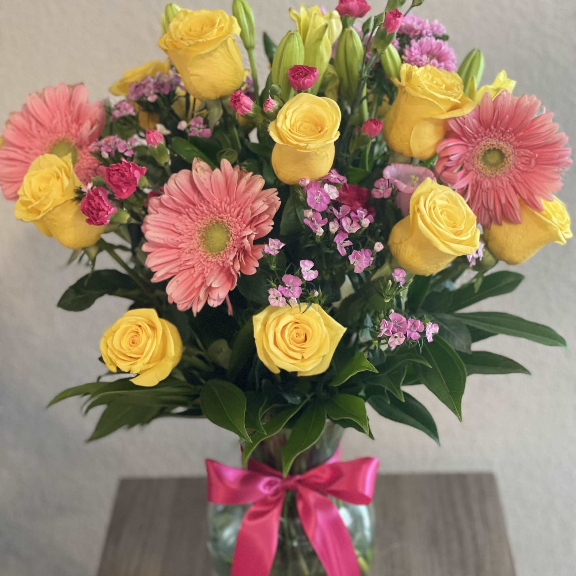 Bouquet of yellow roses and pink gerbera daisies in a glass vase with a pink ribbon