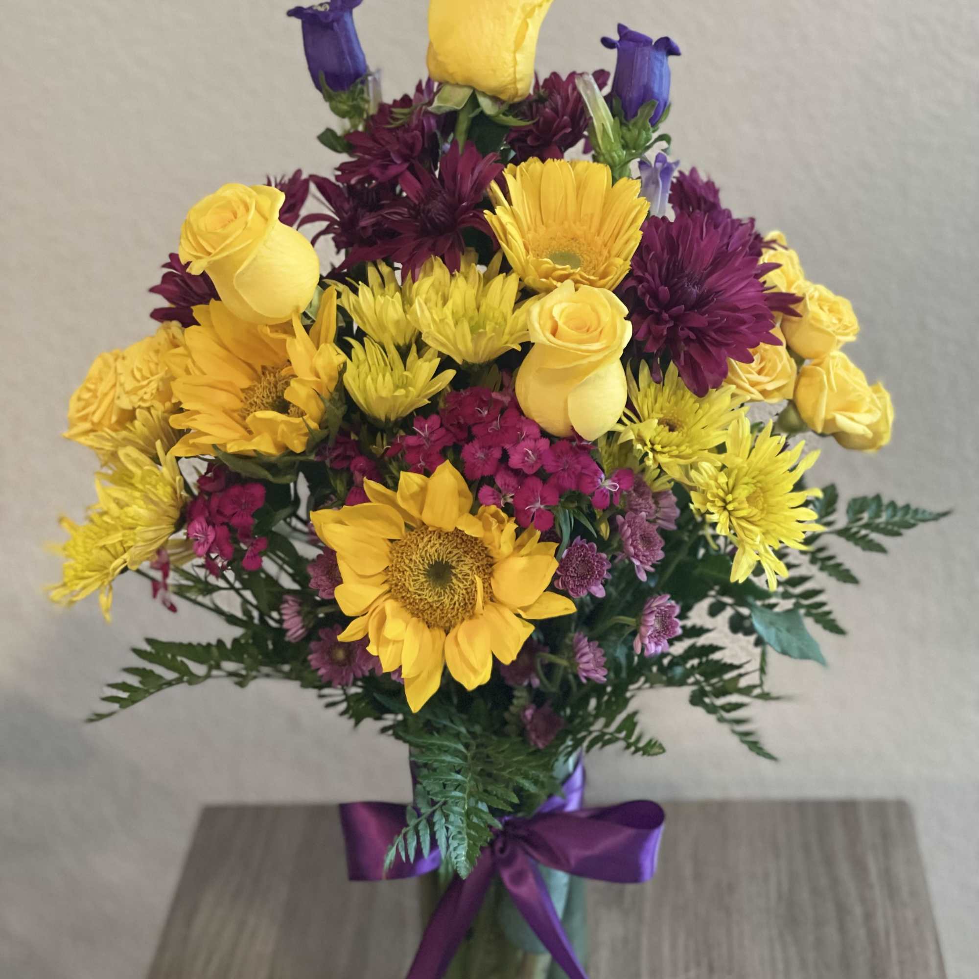Bouquet of yellow roses, sunflowers, and purple blooms in a glass vase