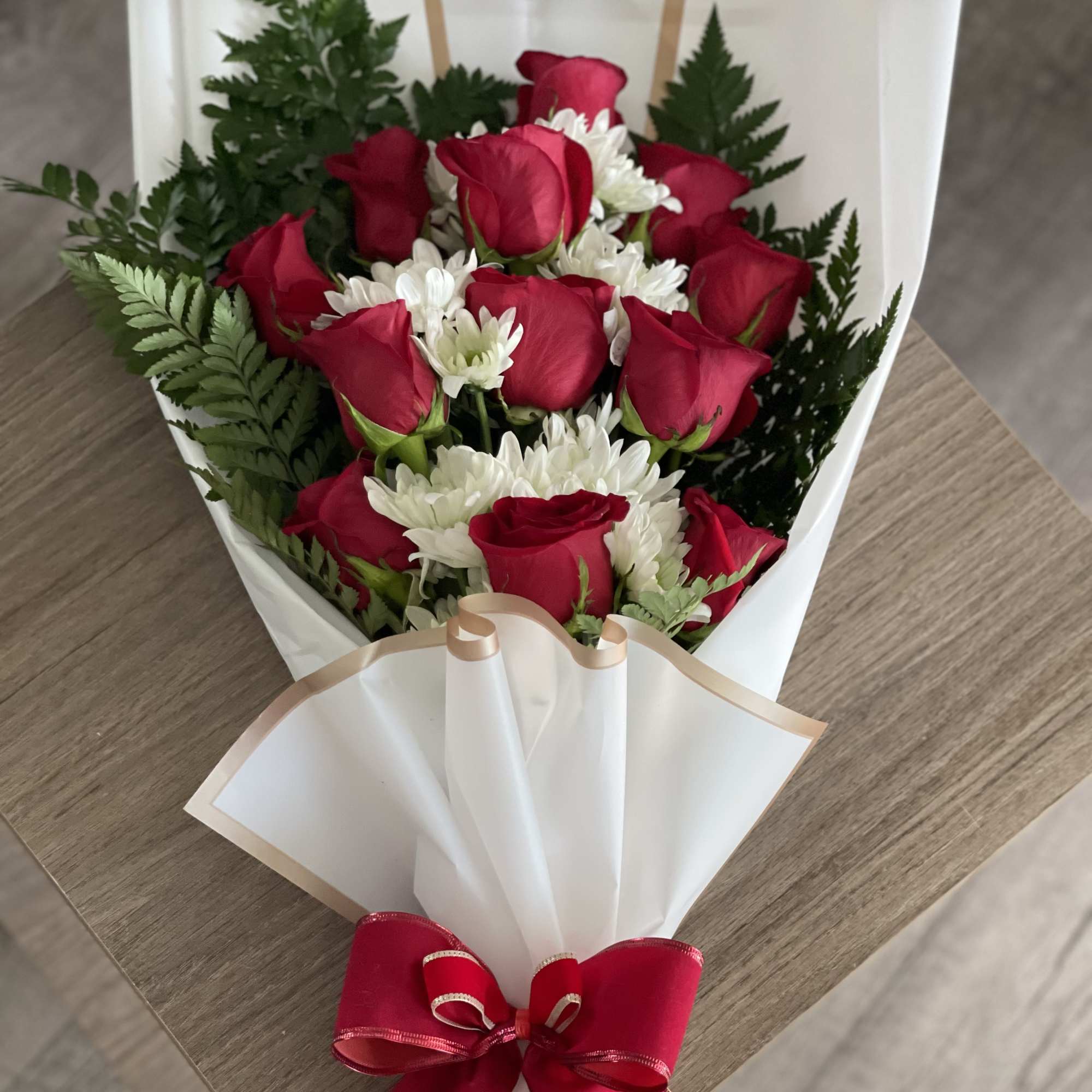 Bouquet of red roses and white daisies wrapped in white paper with a red bow