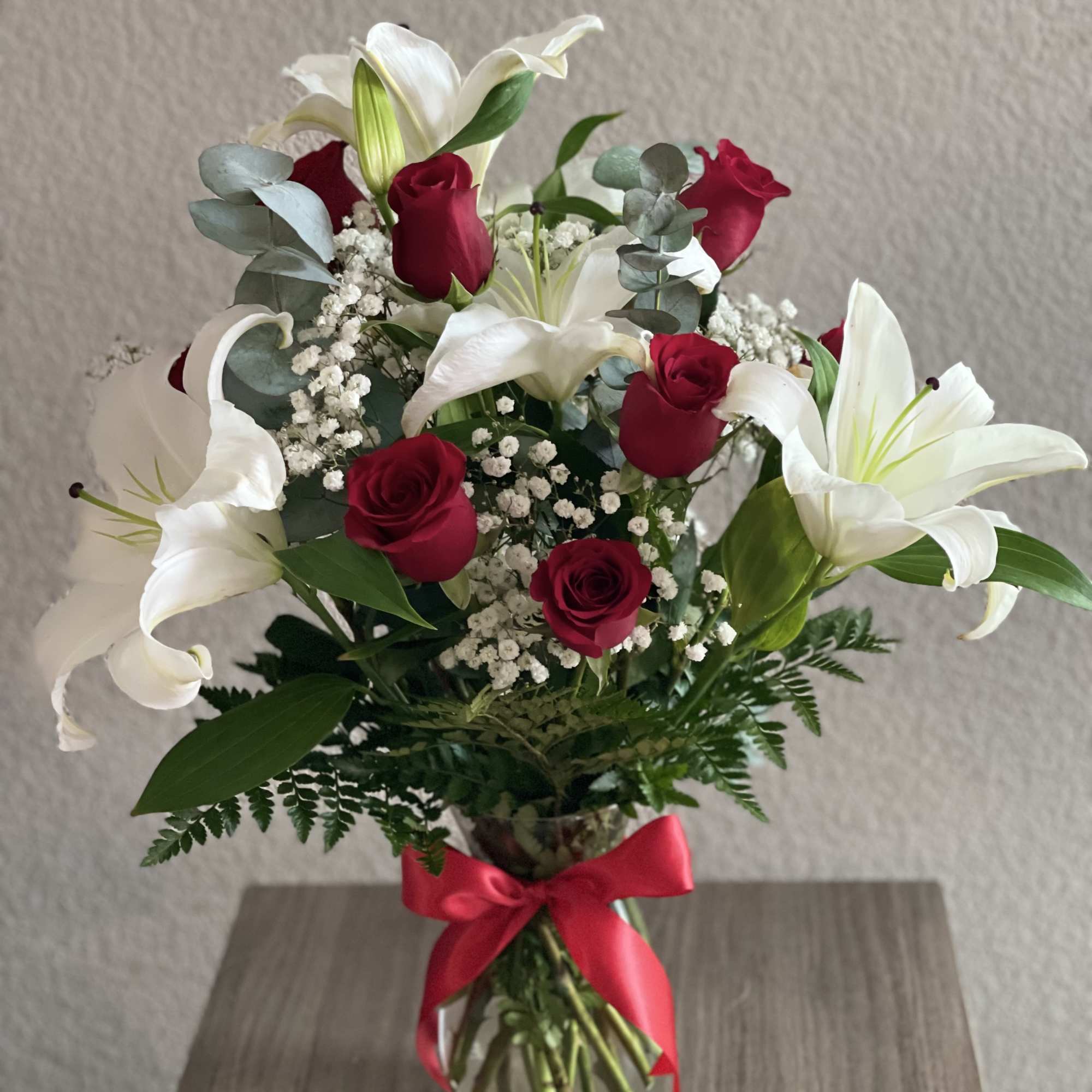Bouquet of red roses and white lilies in a glass vase with a red ribbon
