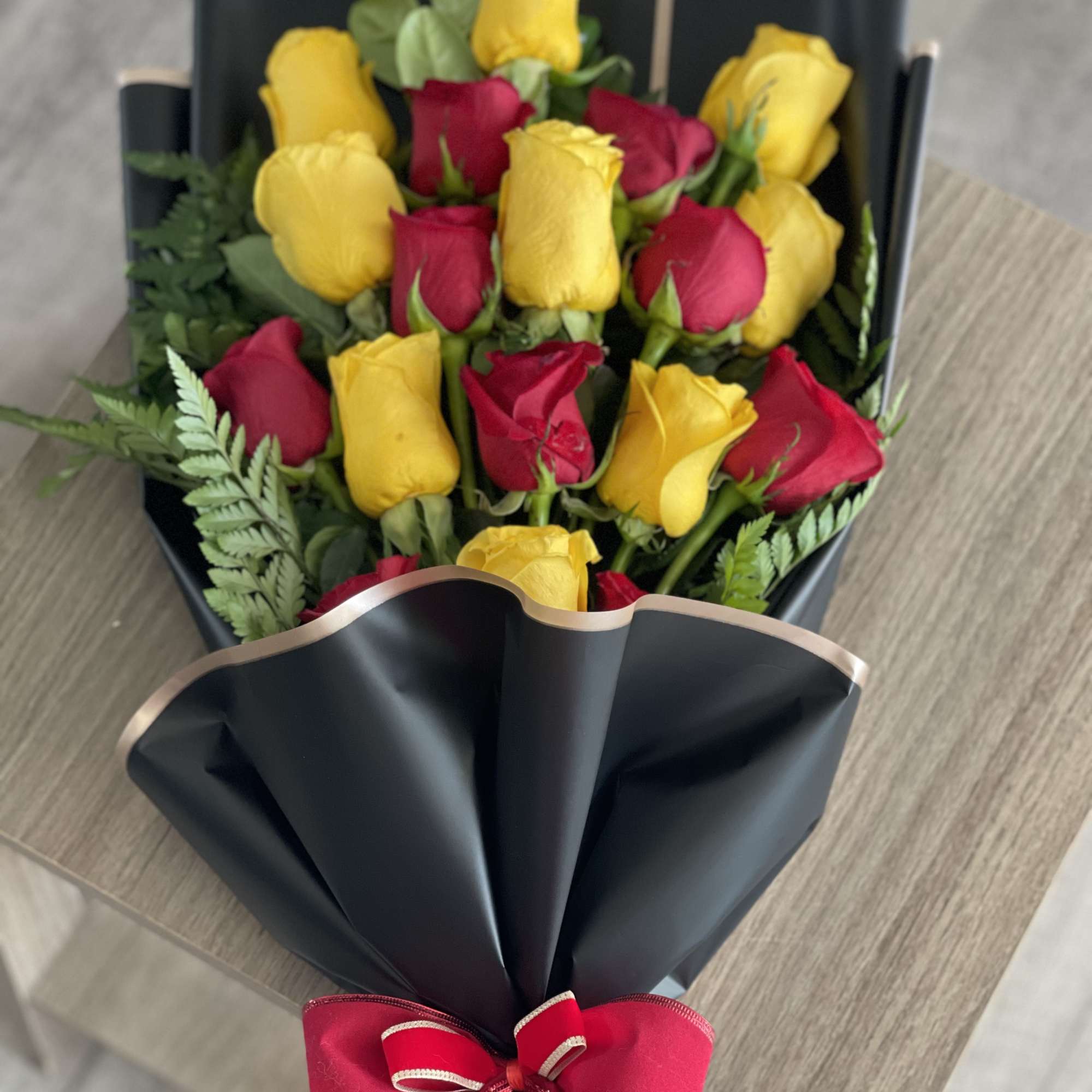 Bouquet of red and yellow roses wrapped in black paper with a red bow