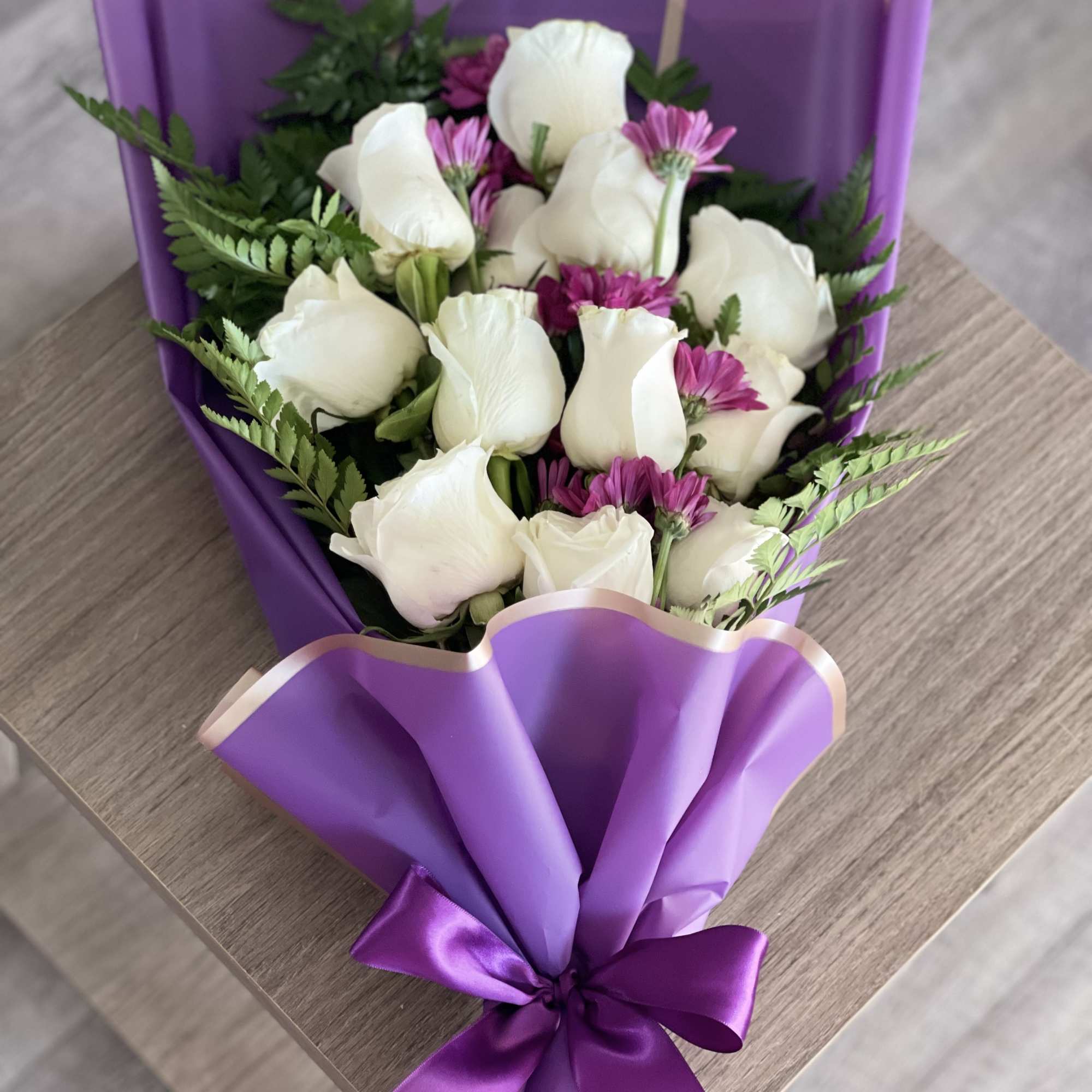 Bouquet of white roses and purple daisies wrapped in purple paper