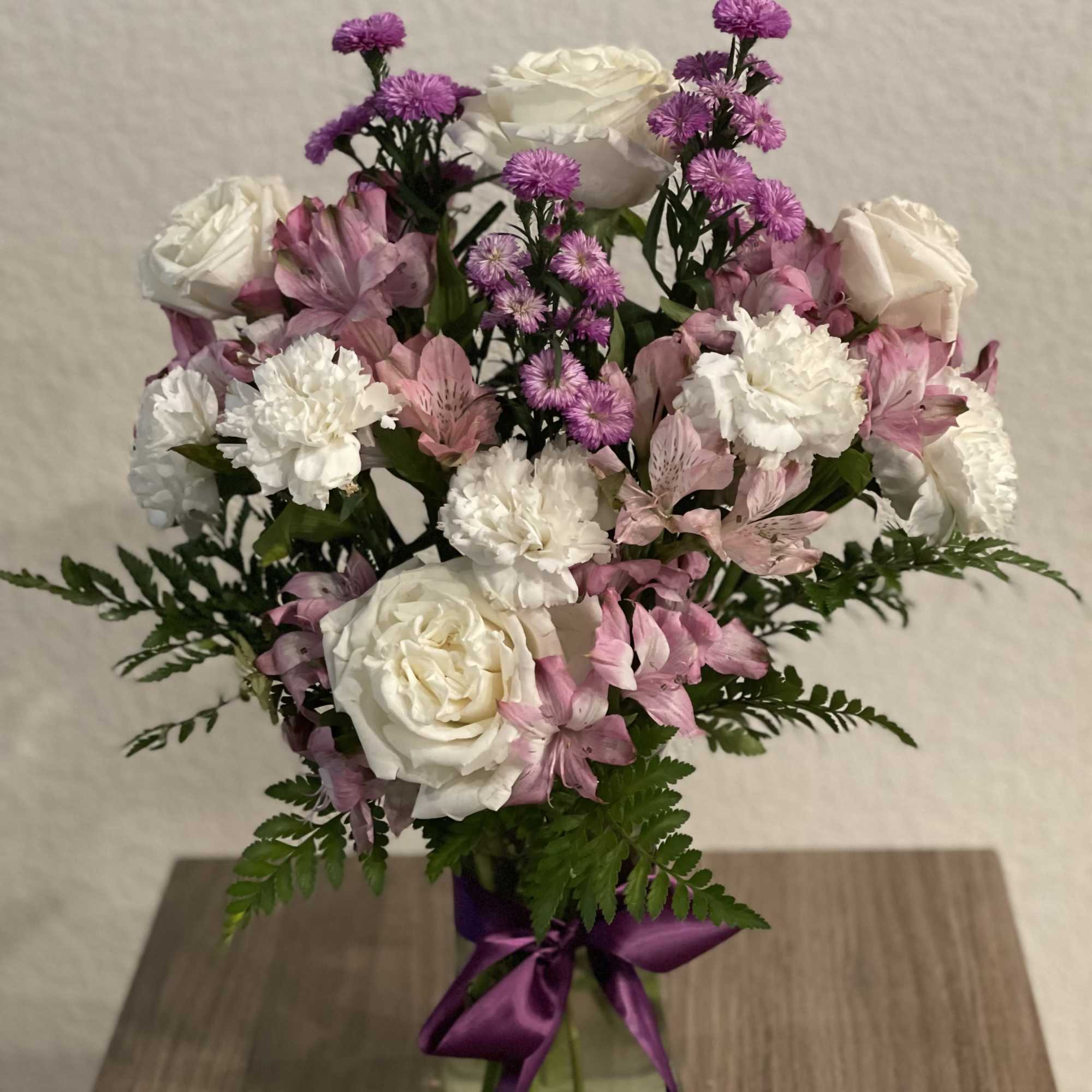 Pink and white bouquet in a glass vase with a purple ribbon