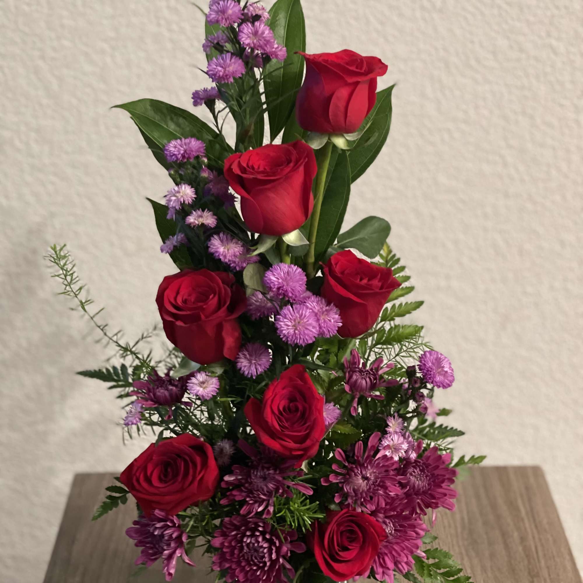 Red roses and purple flowers in a clear glass vase