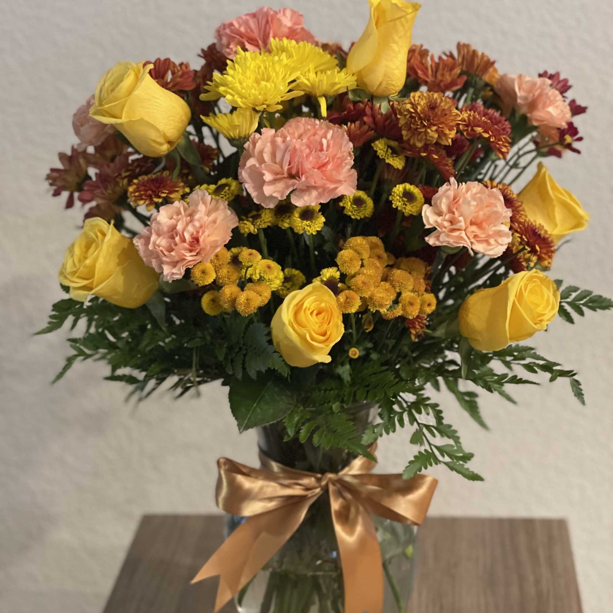 Yellow roses and pink carnations in a glass vase with a gold ribbon