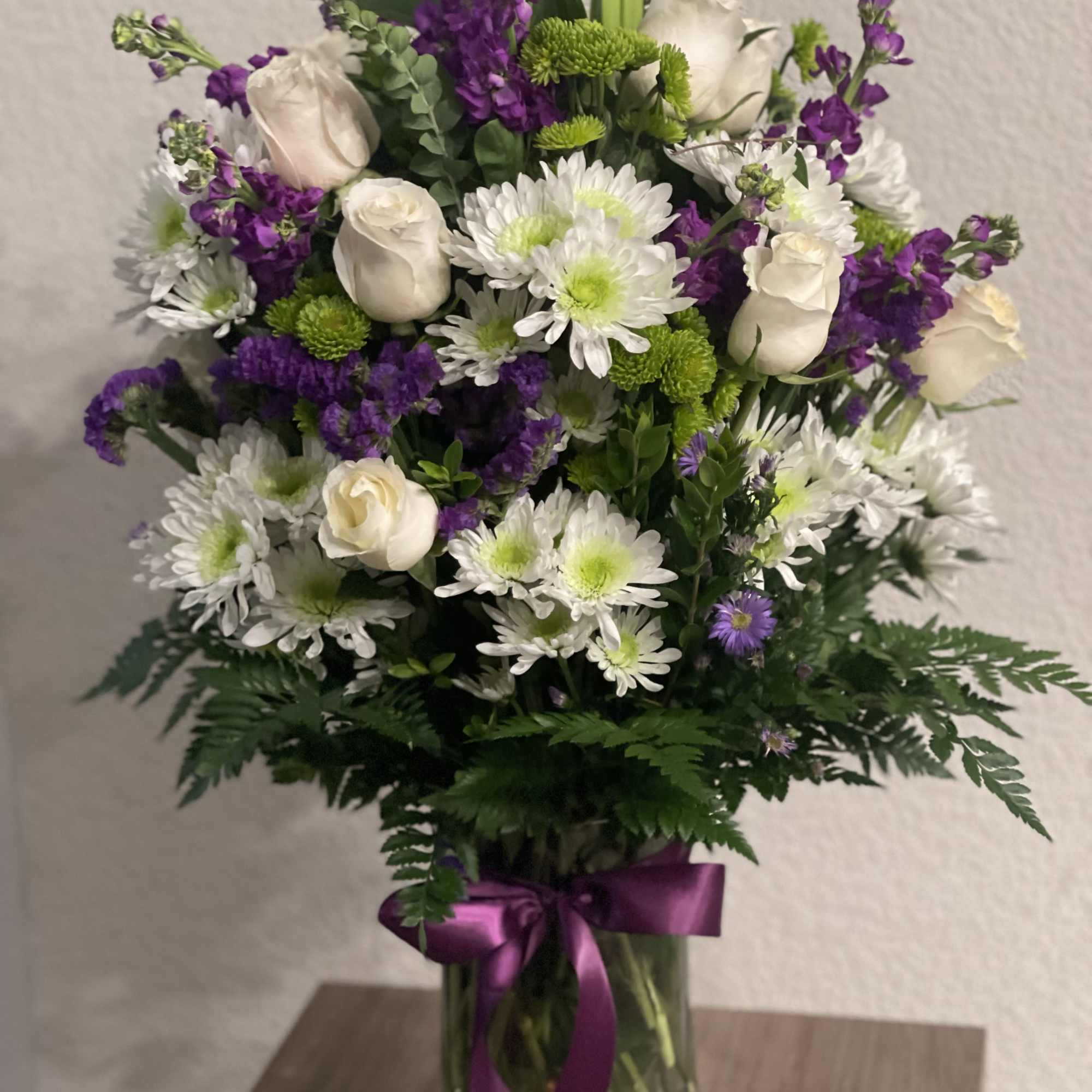 Bouquet of white roses, white daisies, and purple flowers in a glass vase