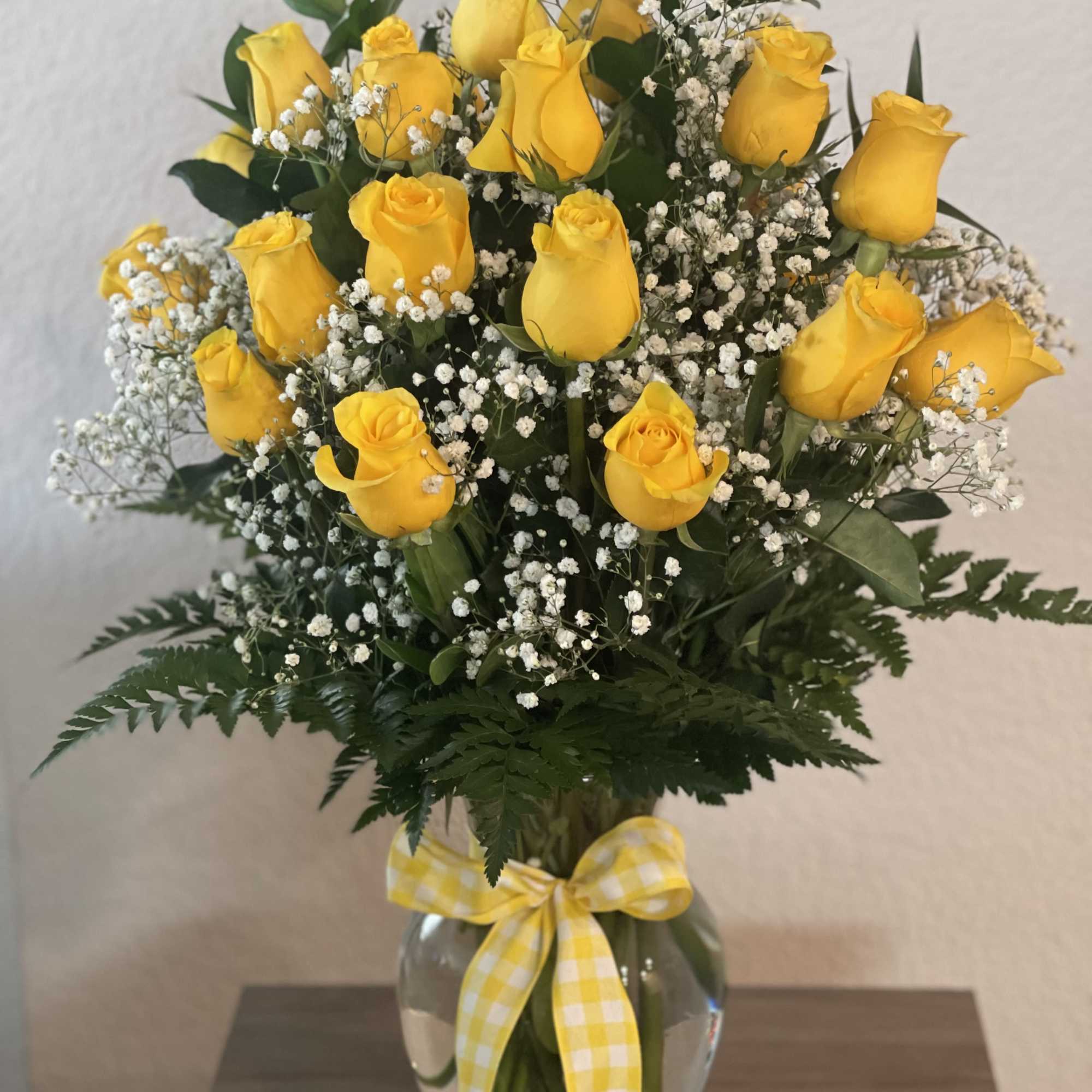 Yellow roses in a clear glass vase with white baby's breath and a gingham ribbon