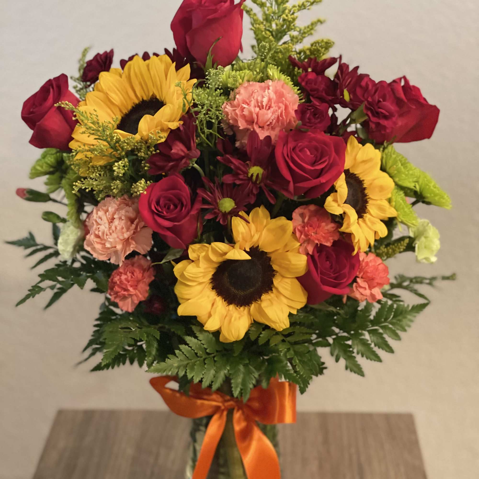 Bouquet of red roses, sunflowers, and carnations in a glass vase with orange ribbon