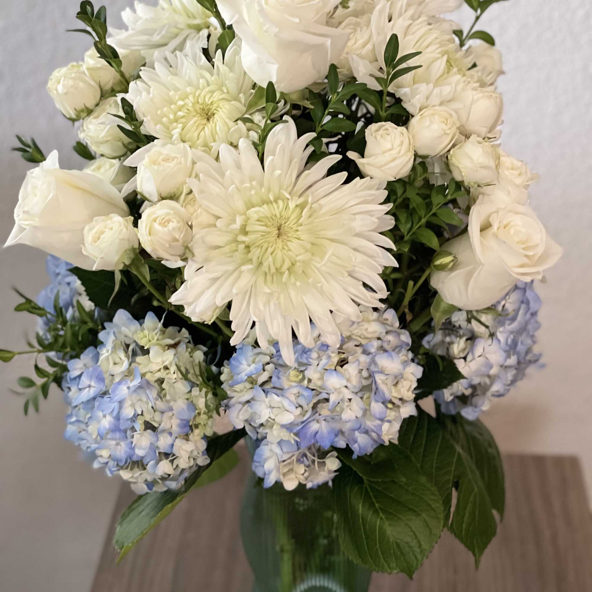 White roses and chrysanthemums with blue hydrangeas in a green glass vase