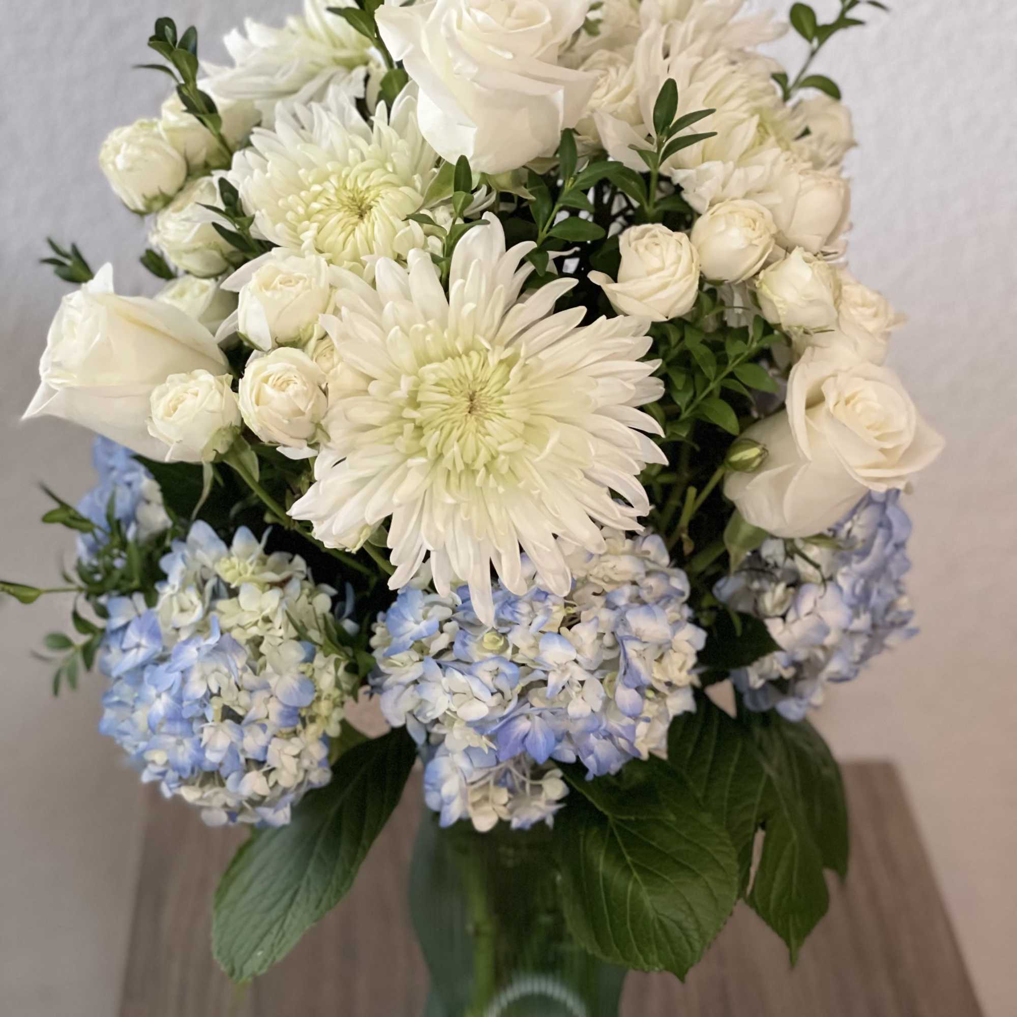 White roses and chrysanthemums with pale blue hydrangeas in a green glass vase