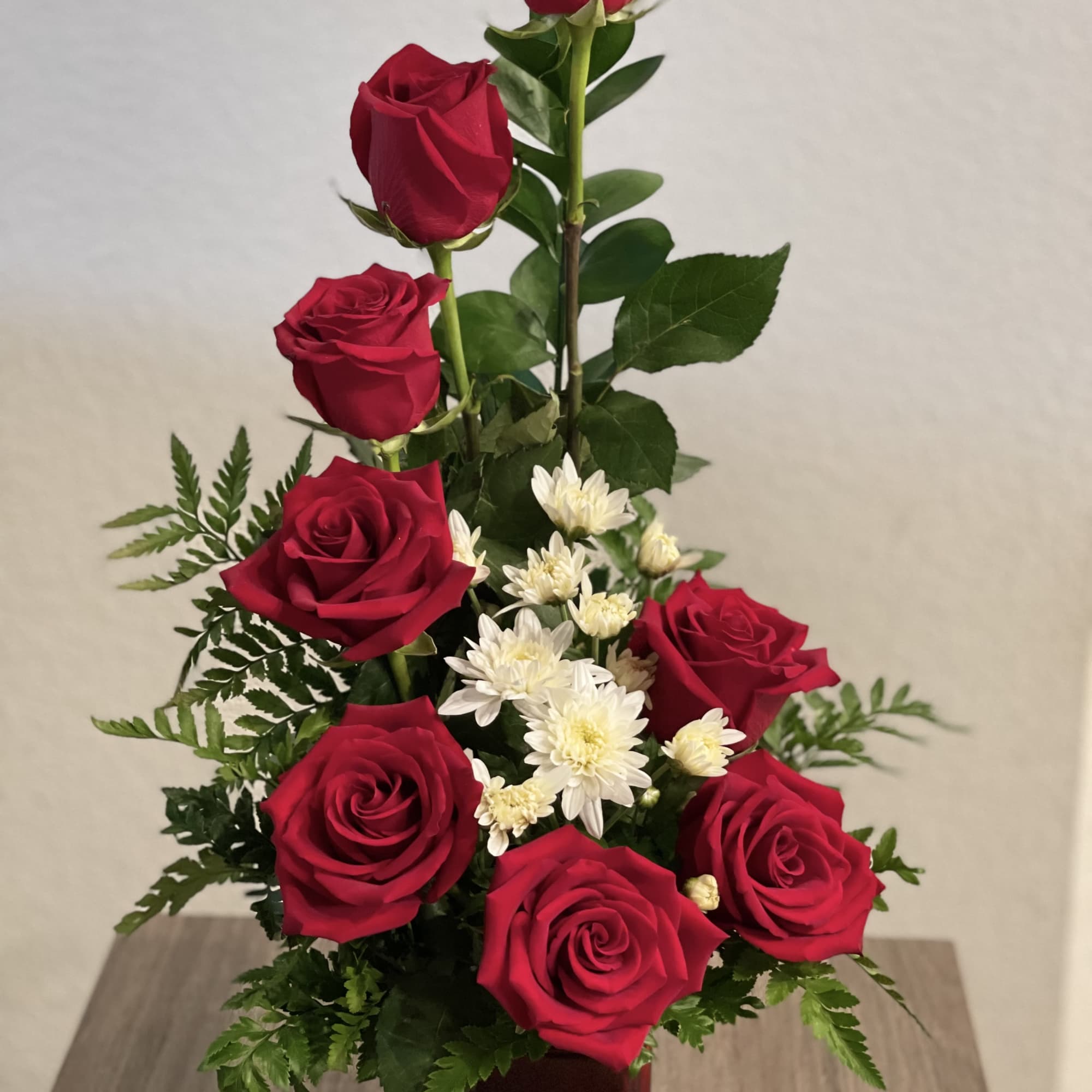 Red roses and white daisies arranged in a square vase