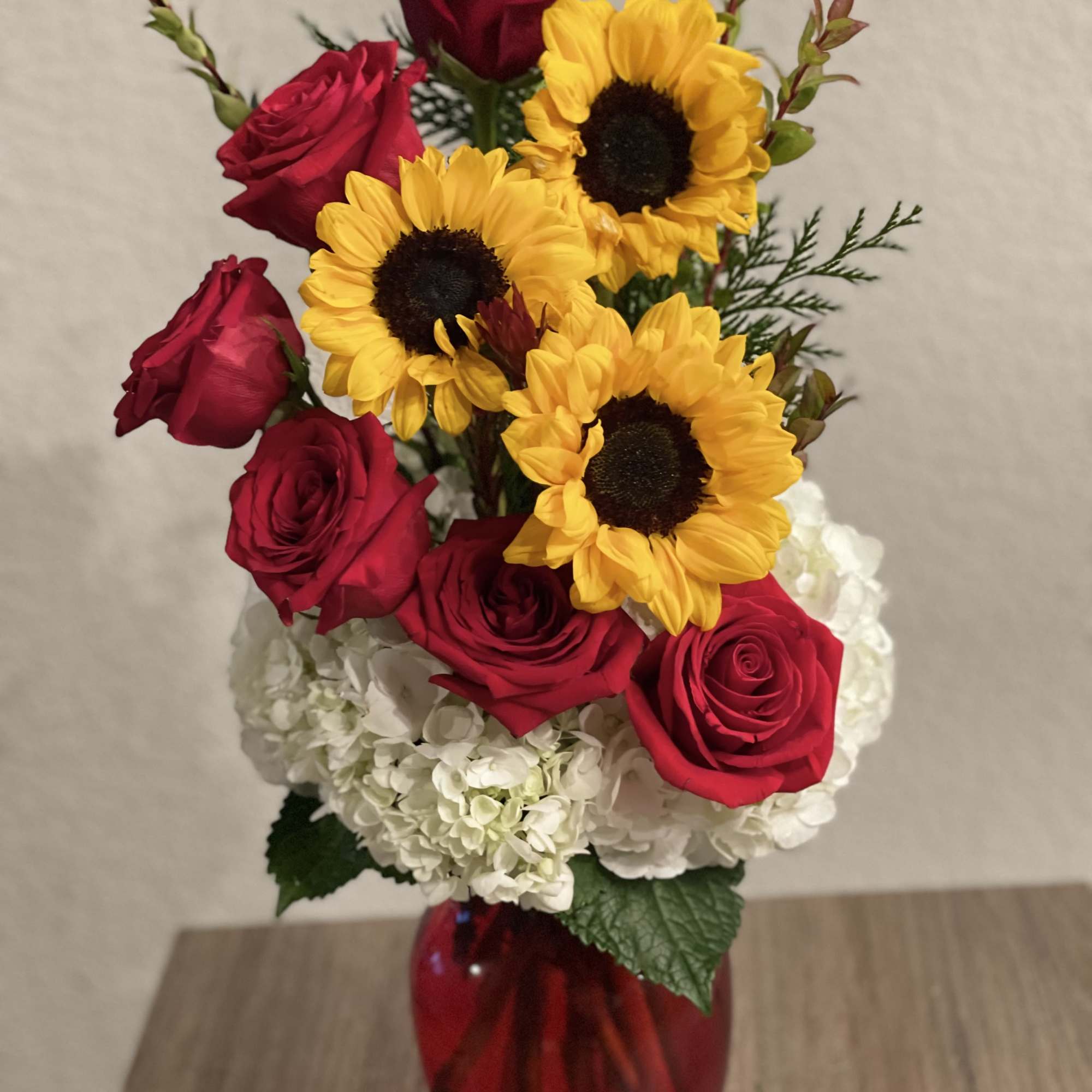 Red roses and yellow sunflowers in a red vase with white hydrangeas