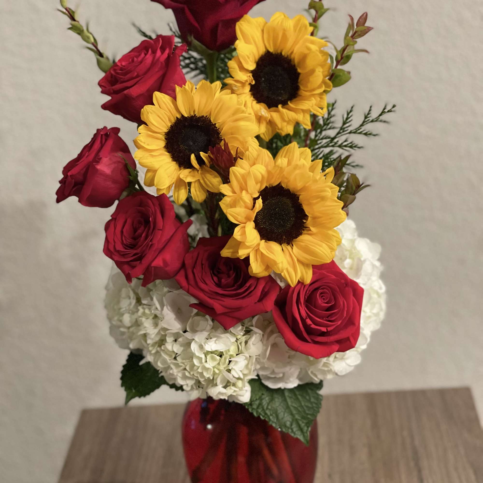 Red roses and yellow sunflowers in a red glass vase