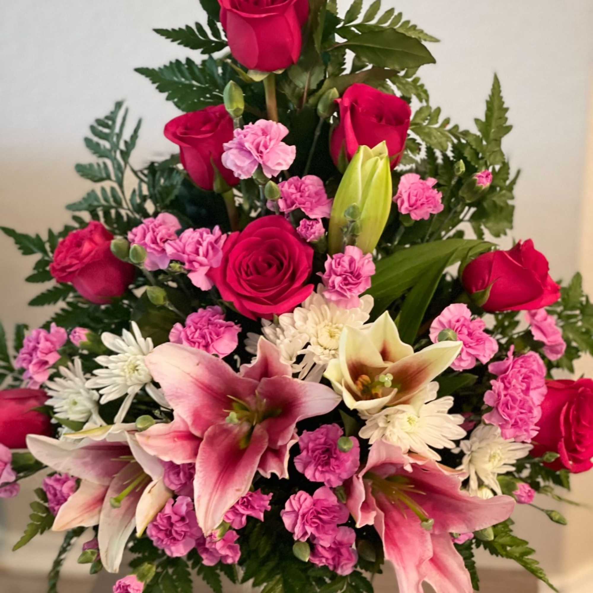 Pink roses and lilies arranged in a clear vase with white daisies and pink carnations