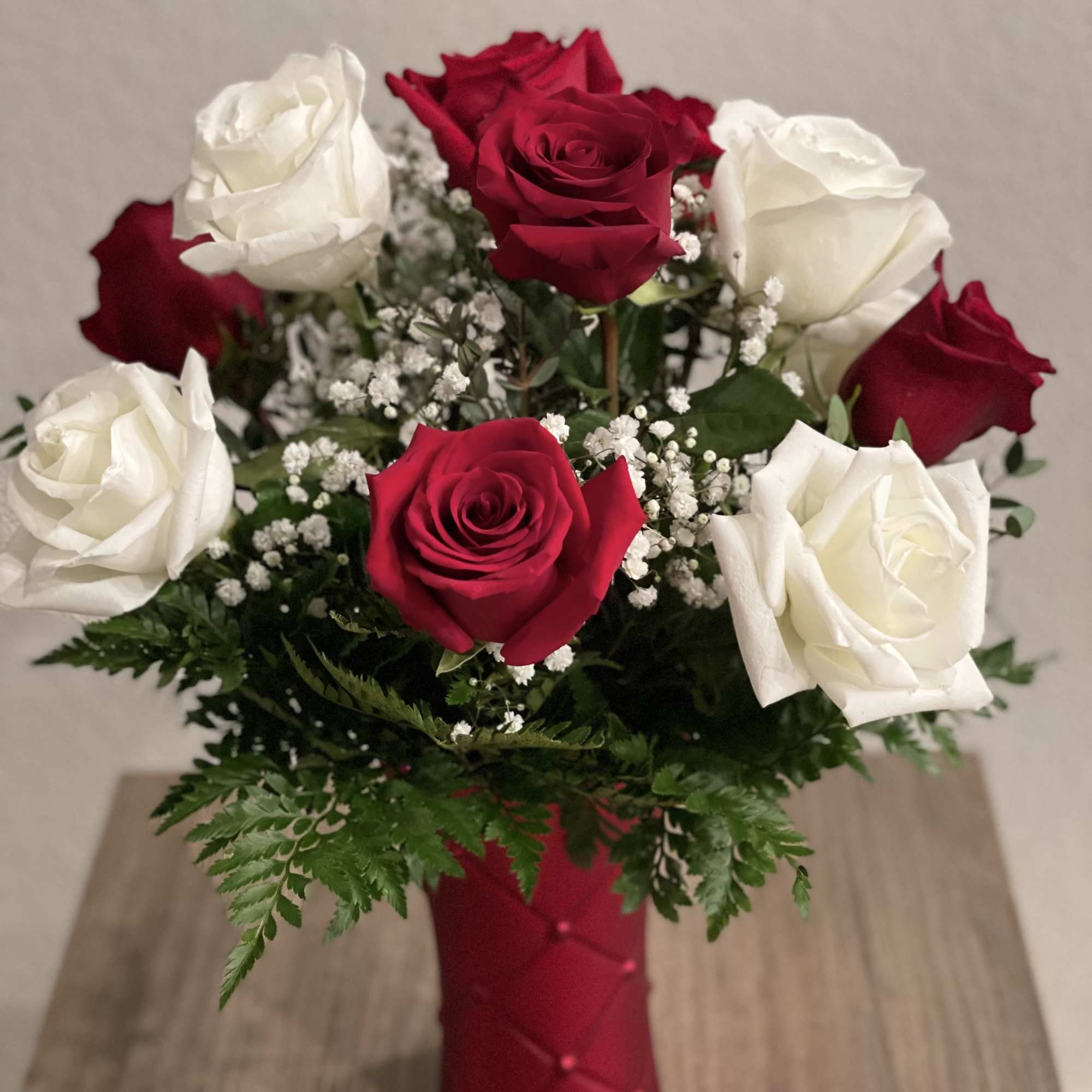 Red and white roses in a red vase with baby's breath