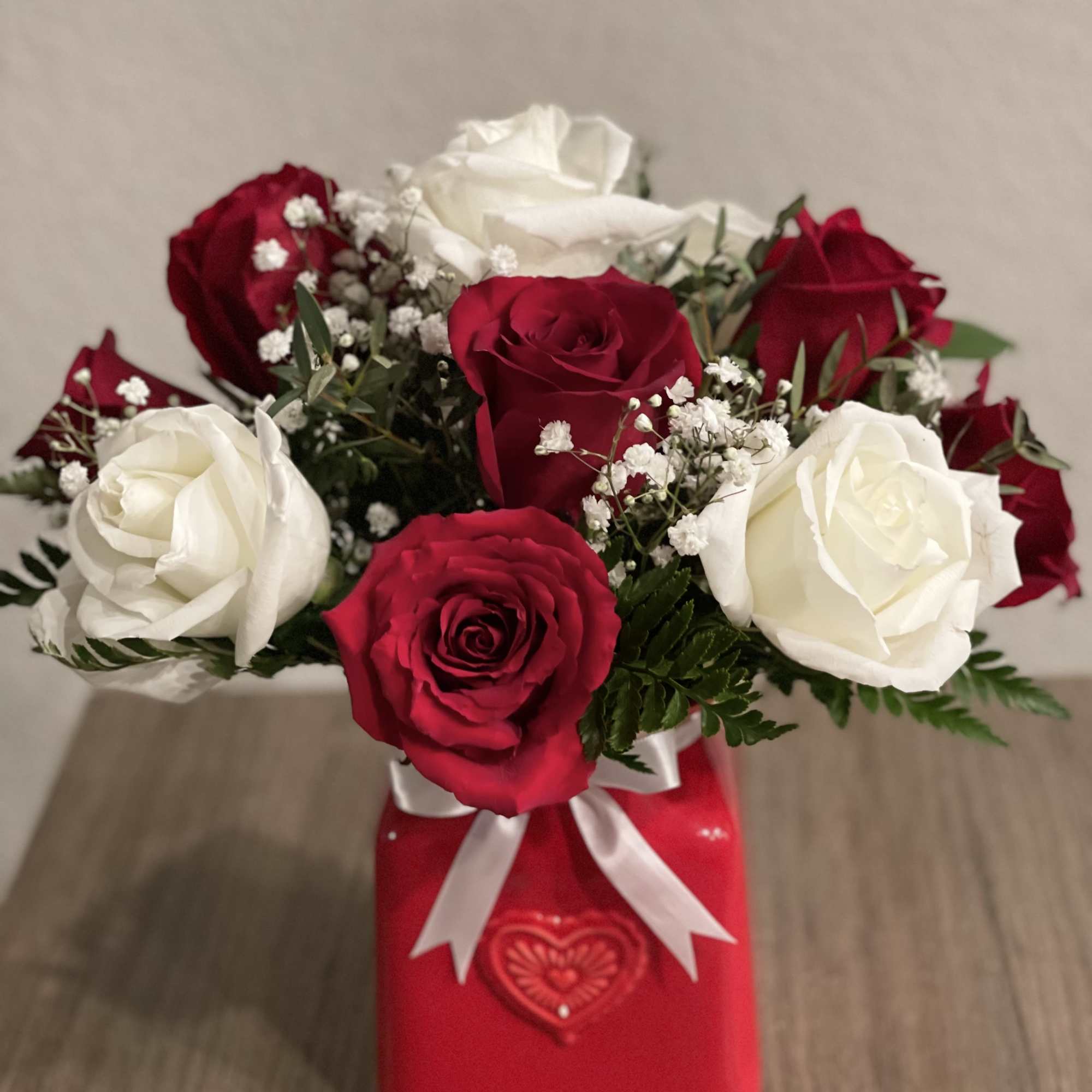 Red and white roses arranged in a red gift box with a white ribbon