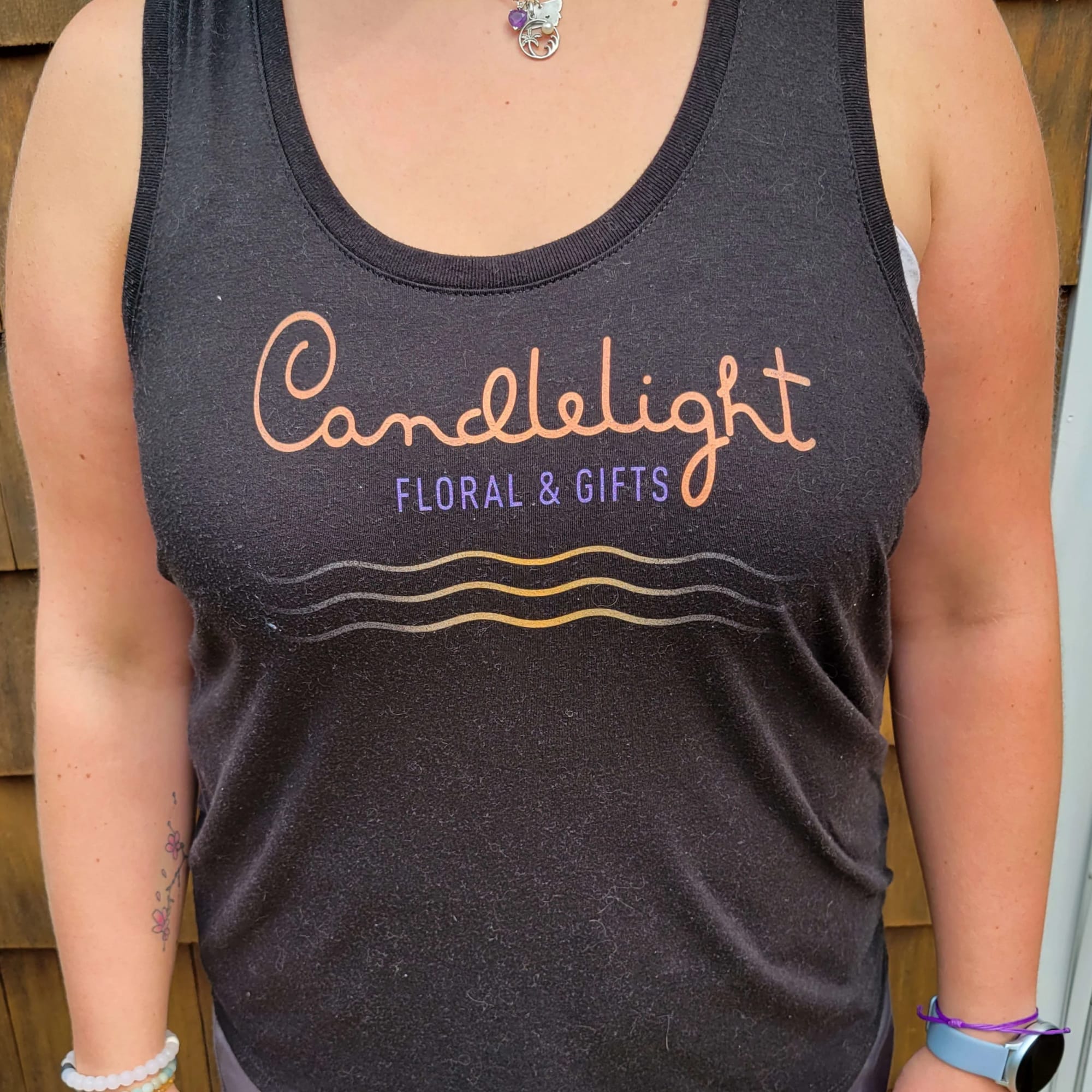 Person wearing a black tank top with a floral shop logo