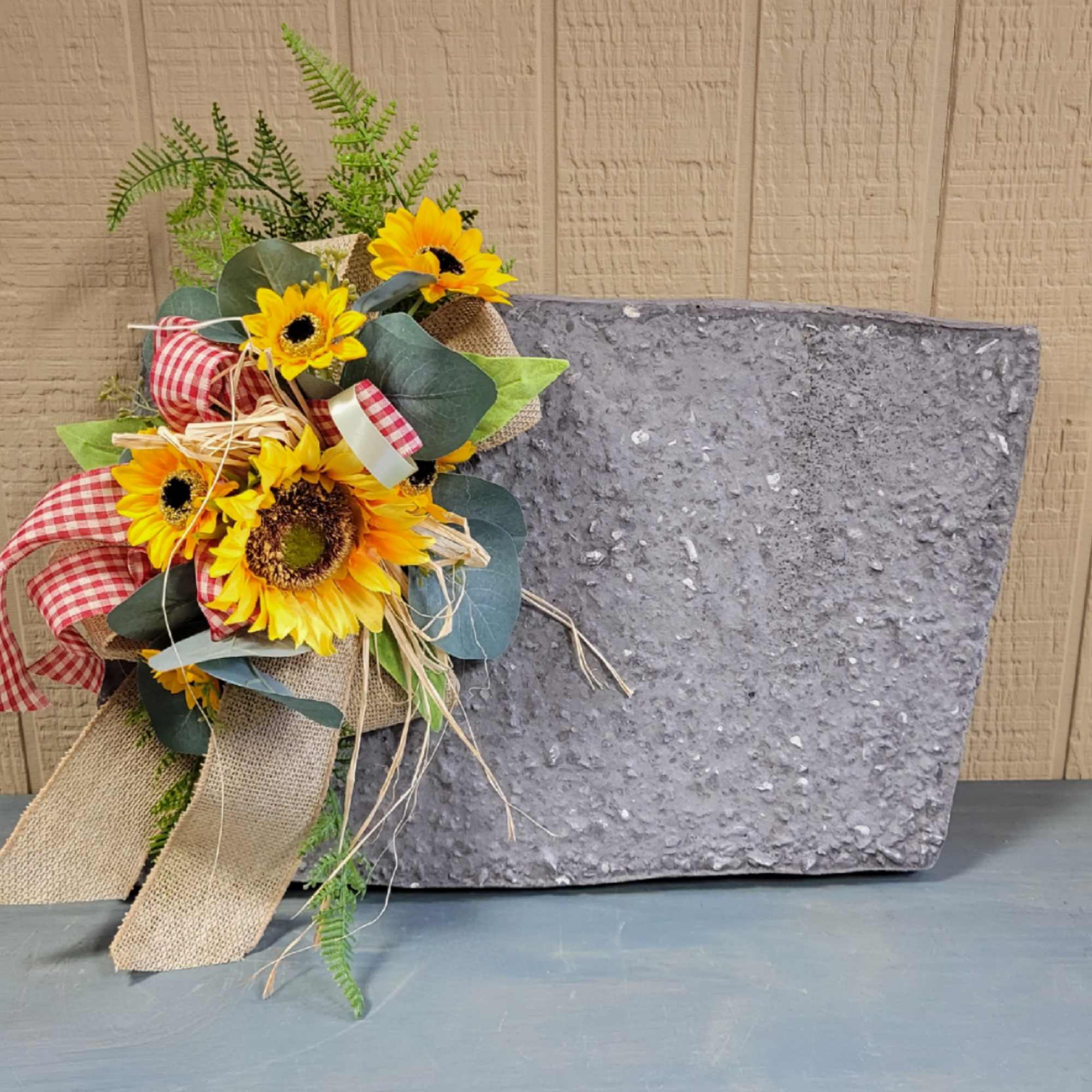 Sunflower arrangement with burlap and gingham ribbon beside a gray stone plaque