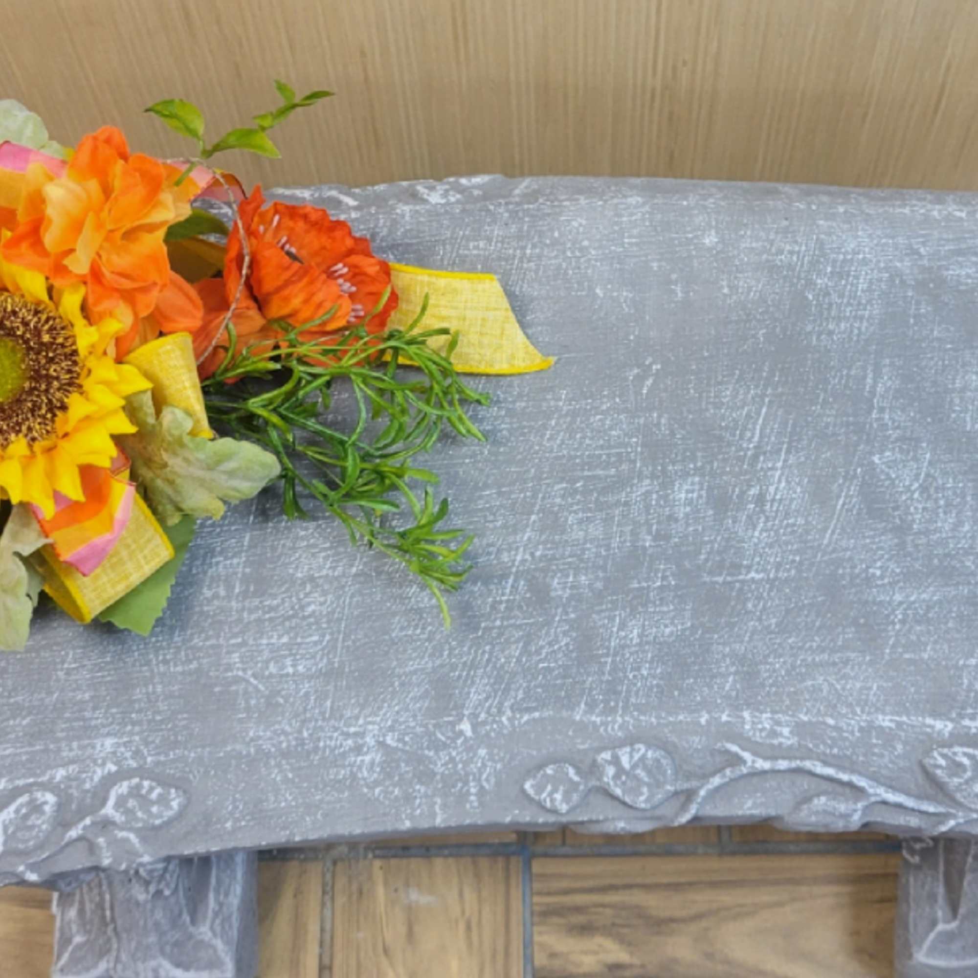 Orange and yellow flower arrangement on a gray bench