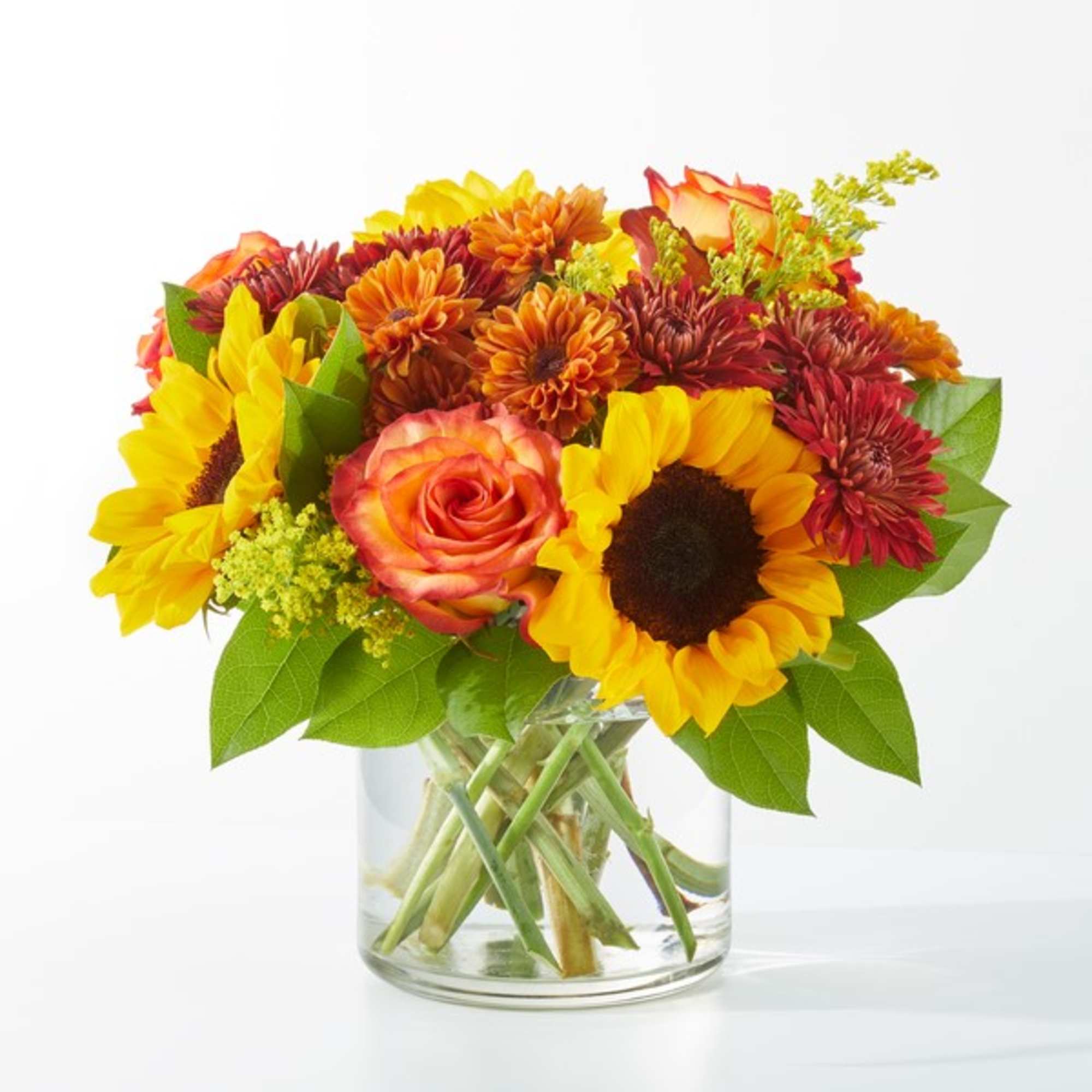 Mixed bouquet of sunflowers, roses, and mums in a clear glass vase