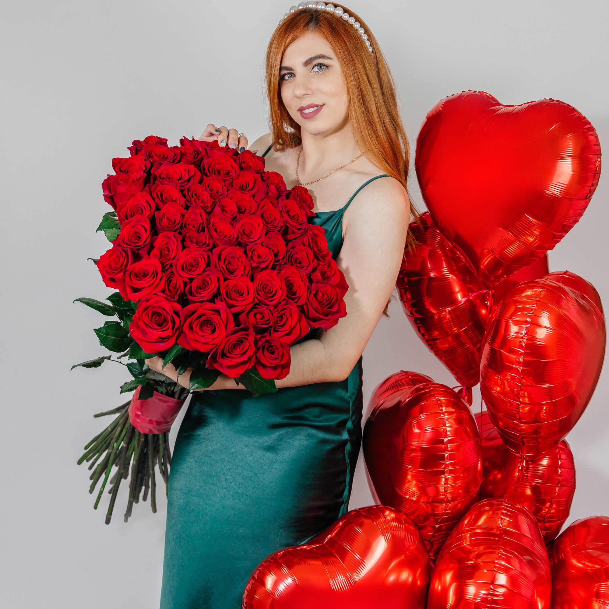 Woman holding a large bouquet of red roses beside red heart balloons