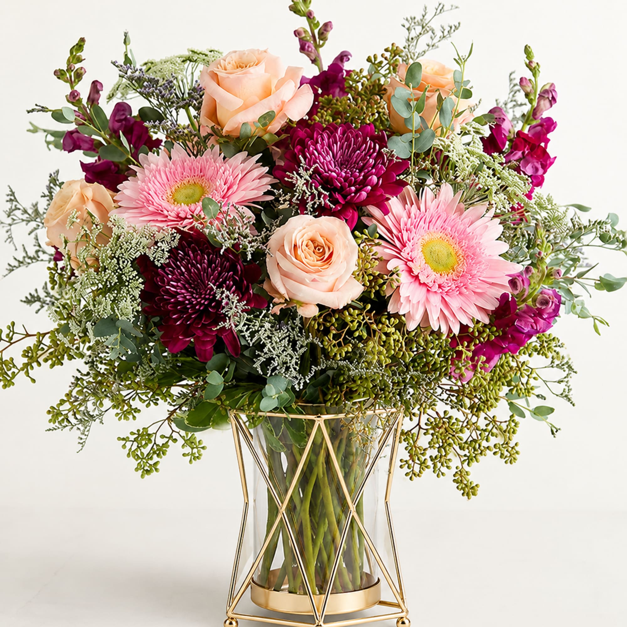 Mixed bouquet of peach roses, pink gerberas, and magenta blooms in a glass vase