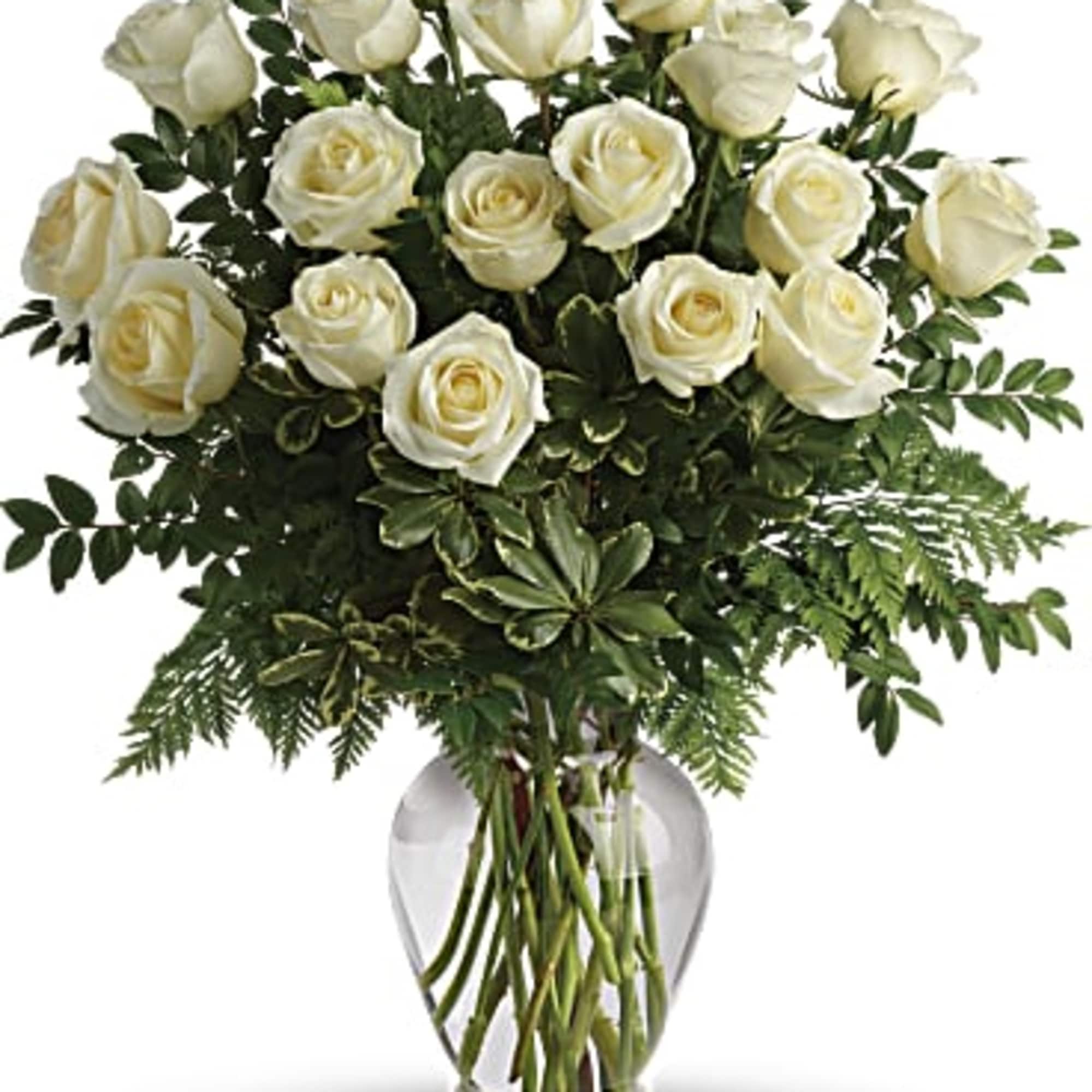 White roses arranged in a clear glass vase with greenery