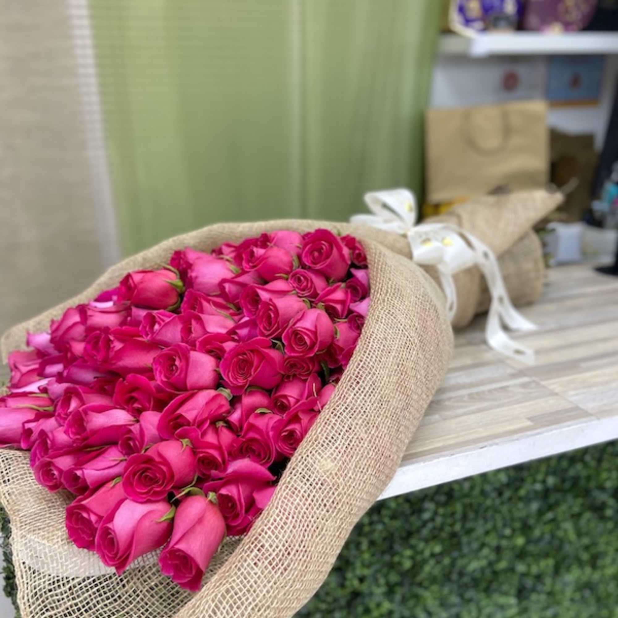Large bouquet of bright pink roses wrapped in burlap and tied with a ribbon on a counter
