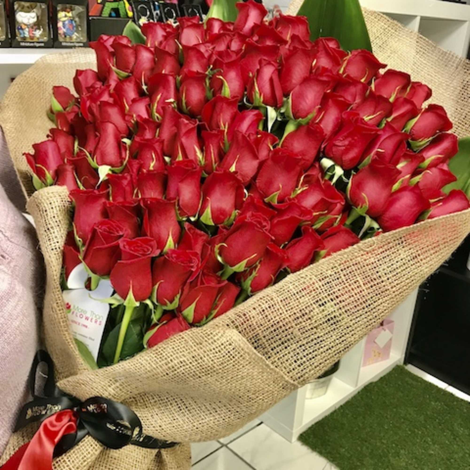 Large bouquet of tightly packed red roses wrapped in burlap and tied with black and red ribbons